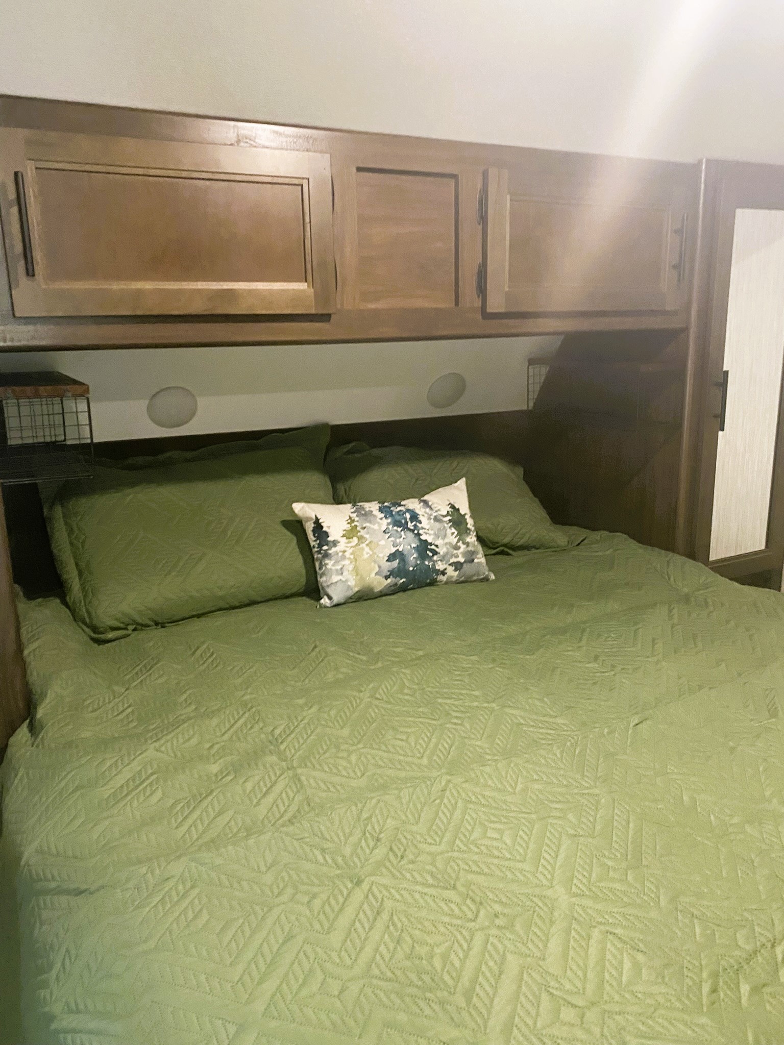 Comfortable RV rental bedroom with green quilted bedding, an accent pillow, overhead cabinets, and wall lights.. Forest River Cherokee Grey Wolf 2020