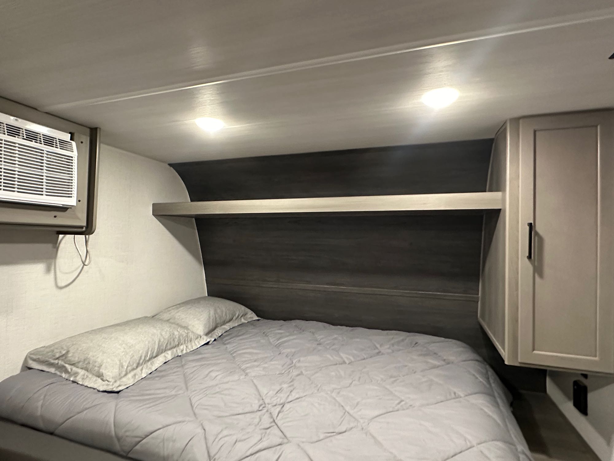 Cozy RV rental bedroom features a gray bed, built-in shelf, AC unit, and storage cabinet, ideal for travel.. Keystone RV Hideout 2024