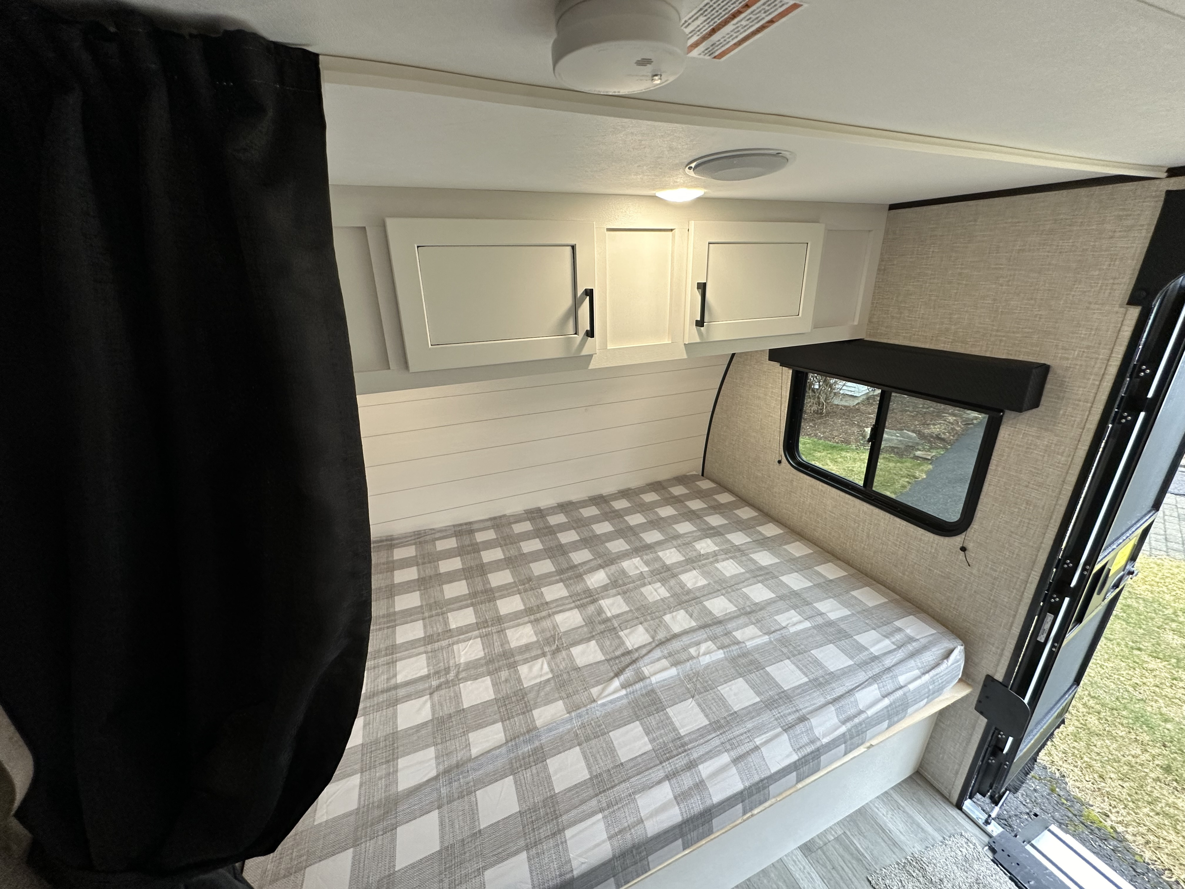 Cozy RV rental bedroom with plaid bed, white shiplap walls, overhead cabinets, black curtain, and a window. Perfect for travel.. Jayco Jay Flight SLX 174 BH 2024