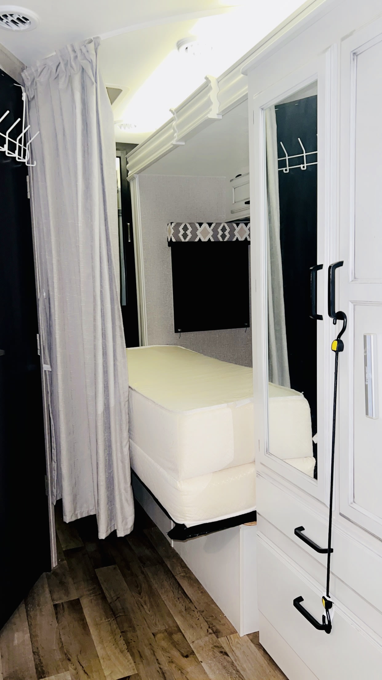 RV rental bedroom: a compact sleeping area with a mattress, grey privacy curtain, mirrored wardrobe, and wood flooring.. Entegra Coach Odyssey 2021