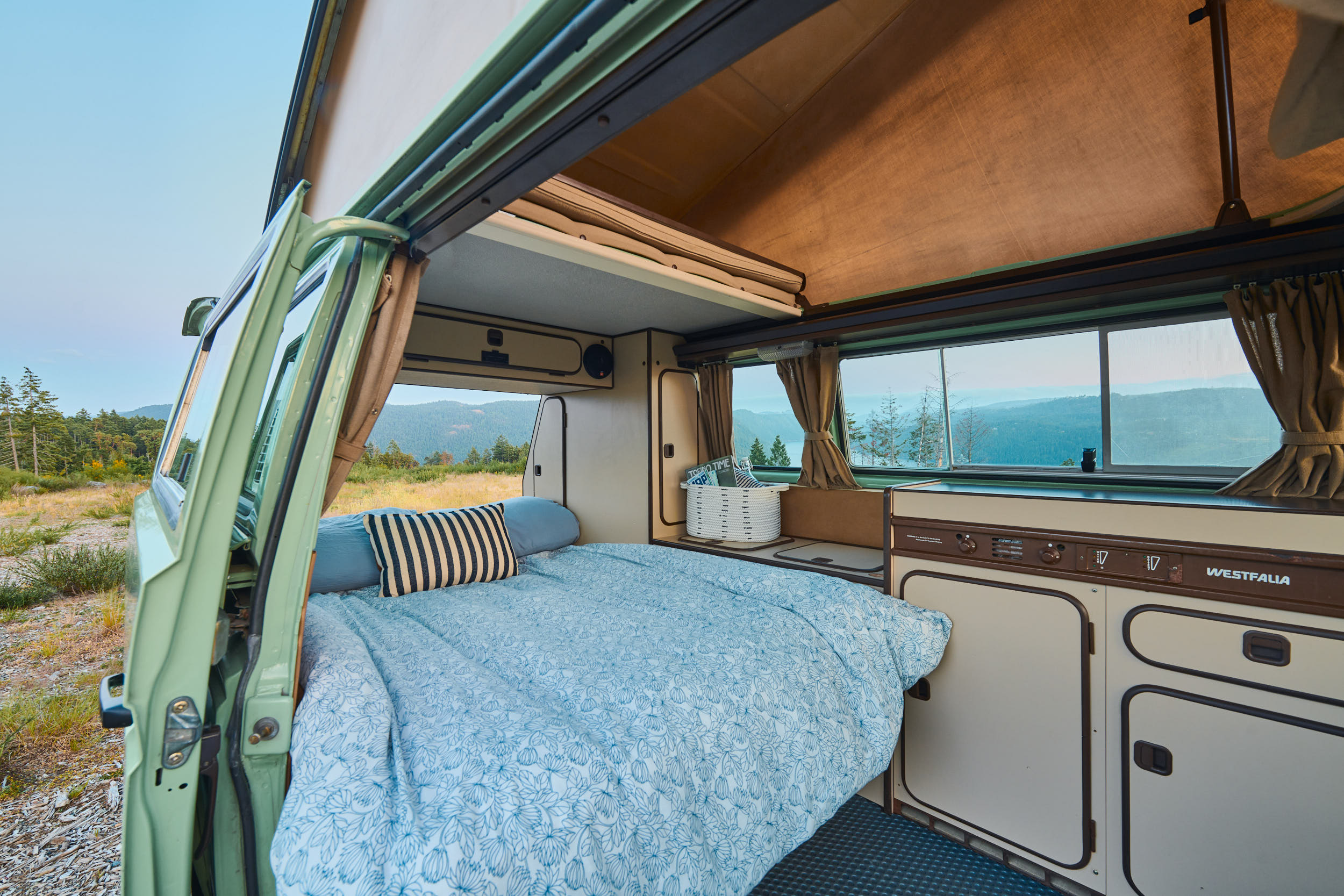 Cozy Westfalia camper interior with a bed, kitchenette, and scenic views. Ideal for your next RV rental trip.. Volkswagen T3 Westfalia 1986