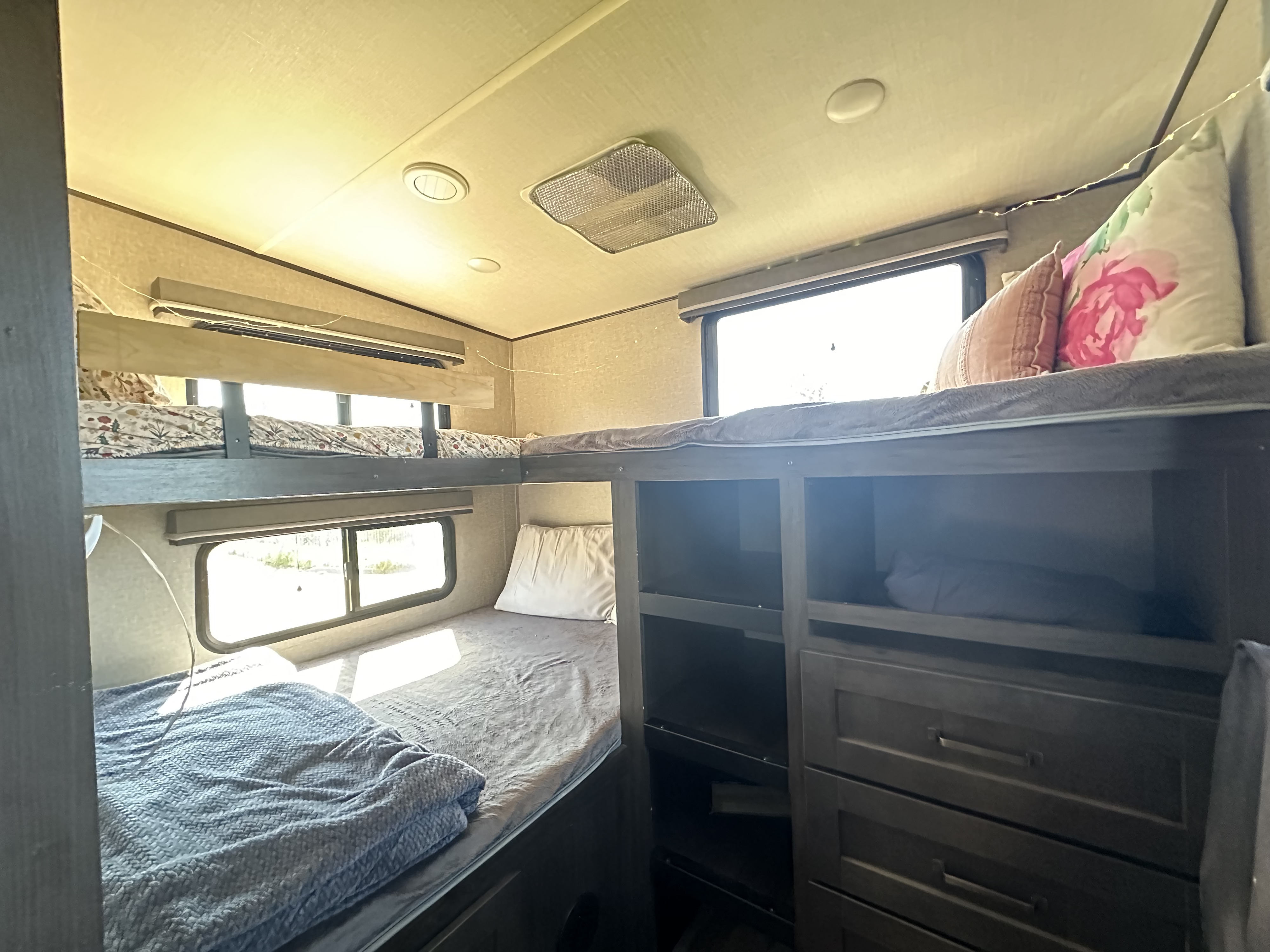 Cozy RV rental interior featuring bunk beds with patterned sheets & pillows, built-in storage, and bright windows.. Grand Design Reflection 2021