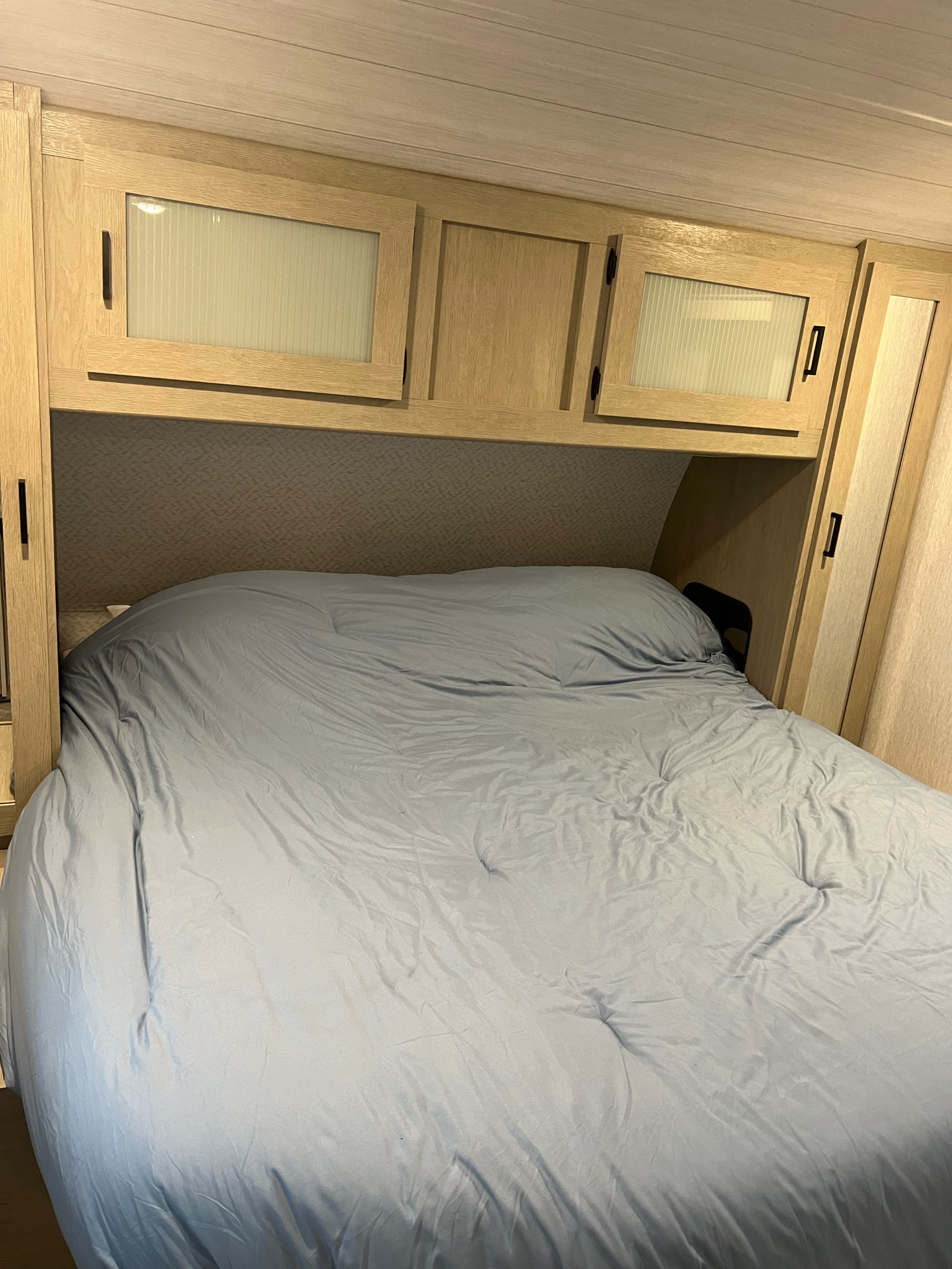 Light blue bedding fills this comfortable RV rental bedroom, featuring overhead wooden cabinets & built-in storage.. Forest River Salem FSX Platinum 2023
