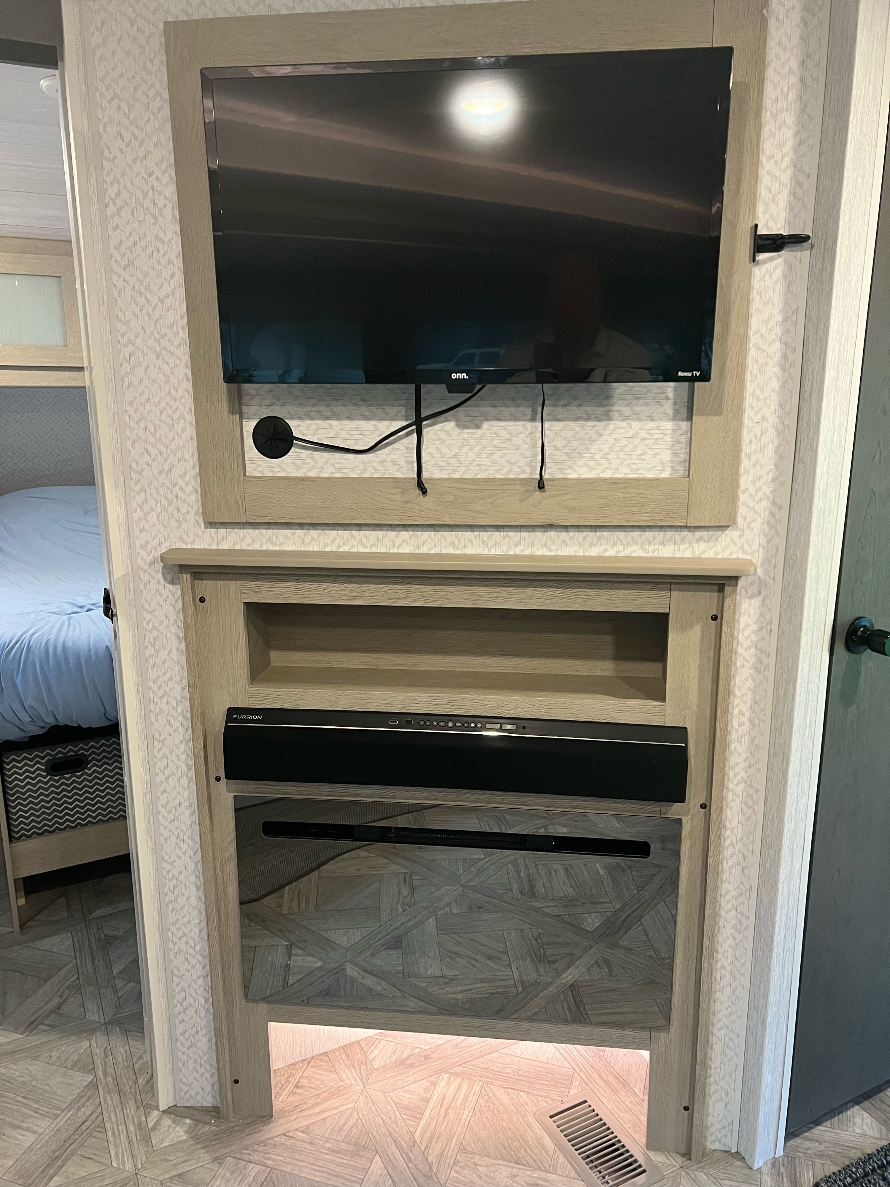 Modern RV rental interior with a wall-mounted TV, soundbar, and electric fireplace, next to a bed.. Forest River Salem FSX Platinum 2023