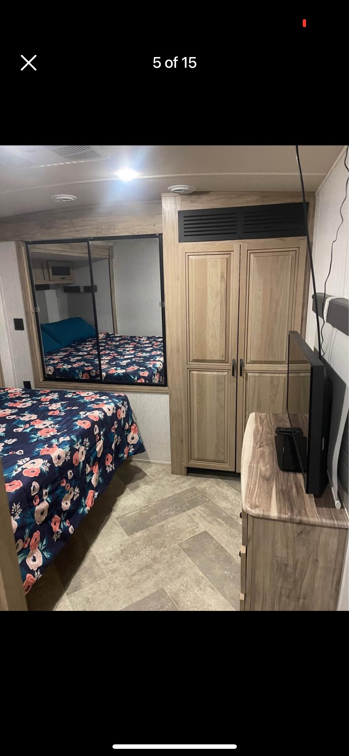 Comfortable RV rental bedroom featuring a floral bed, modern mirrored wall, and built-in storage with TV.. Forest River Palomino Solaire 2021
