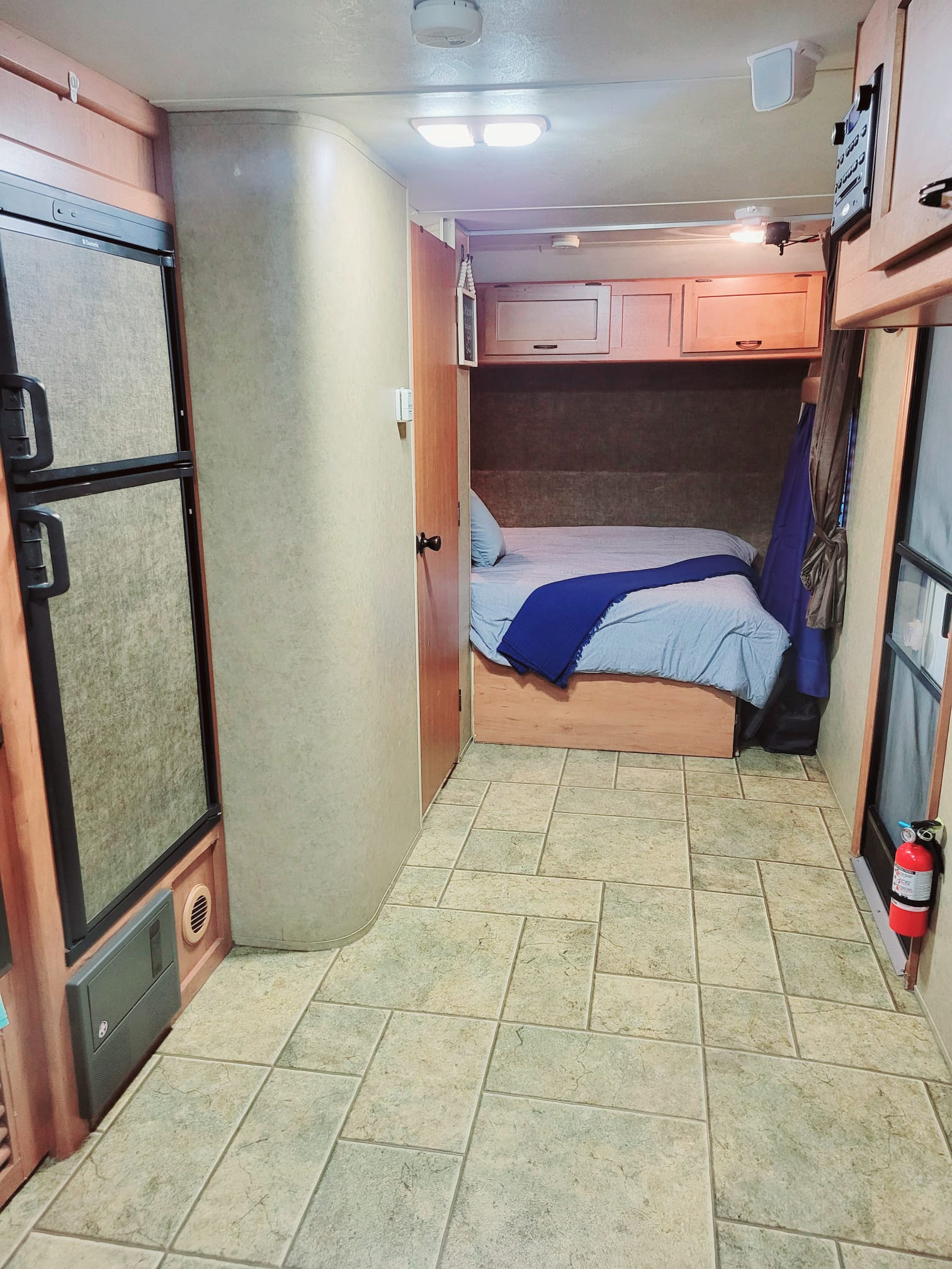 Inside this RV rental: a neat bedroom with a light blue bed, a refrigerator, and light tile flooring. Ready for your next adventure!. Forest River Cherokee Grey Wolf 2014