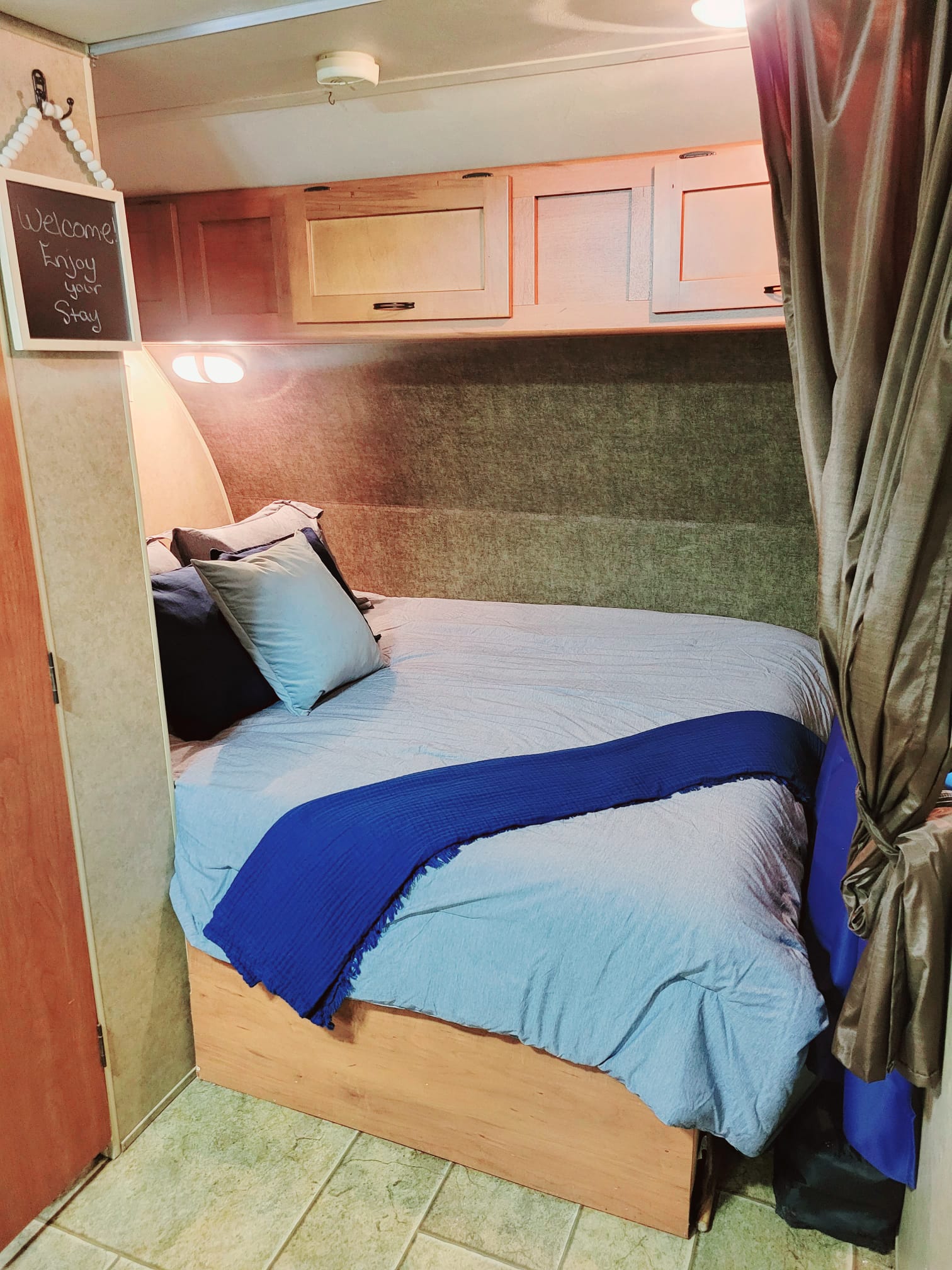 Cozy RV rental bedroom with blue bedding, overhead cabinets, a welcome sign, and a privacy curtain.. Forest River Cherokee Grey Wolf 2014