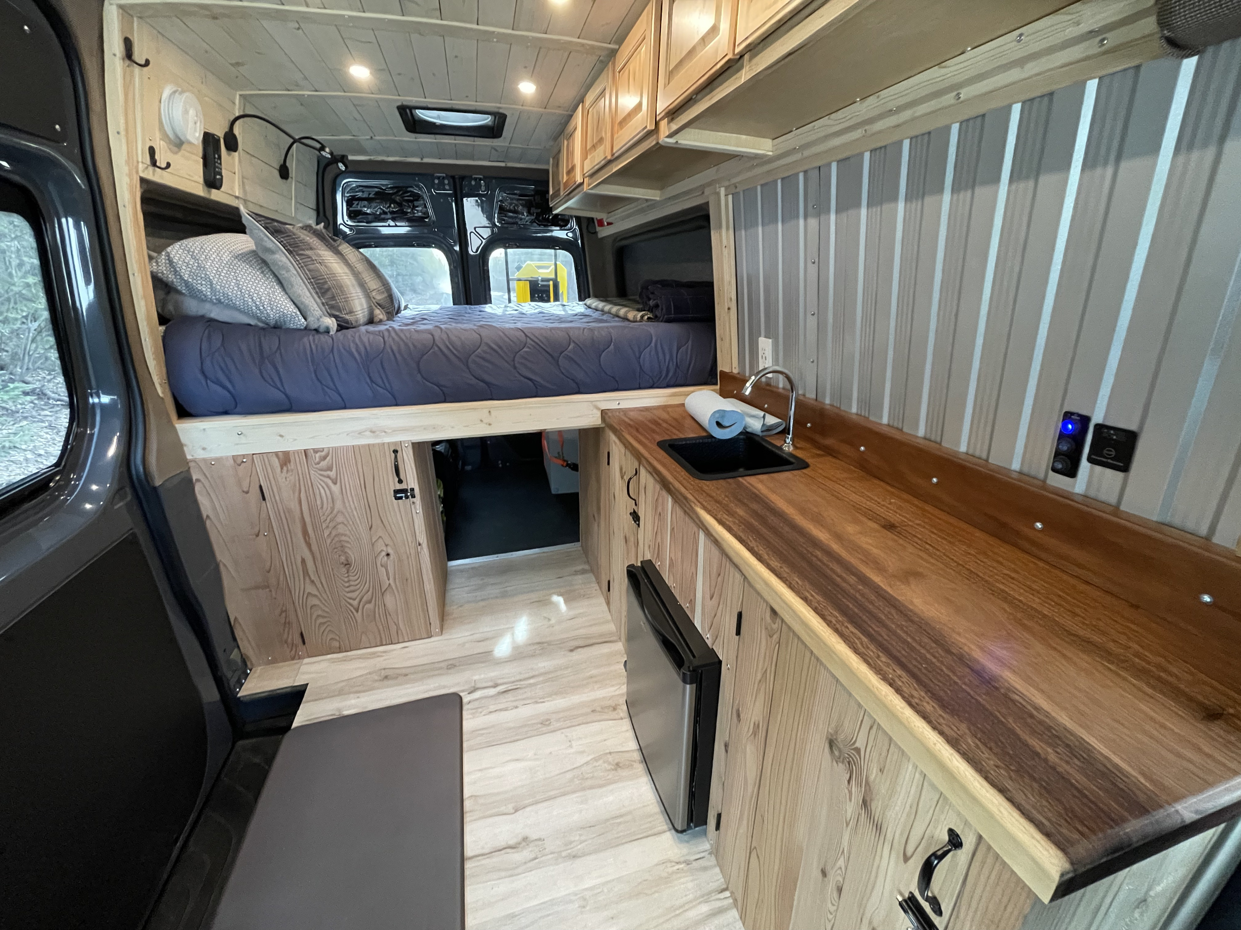 Cozy **rv rental** camper van interior featuring an elevated bed, compact kitchen with sink, fridge, and warm wooden accents.. Mercedes Sprinter 2022