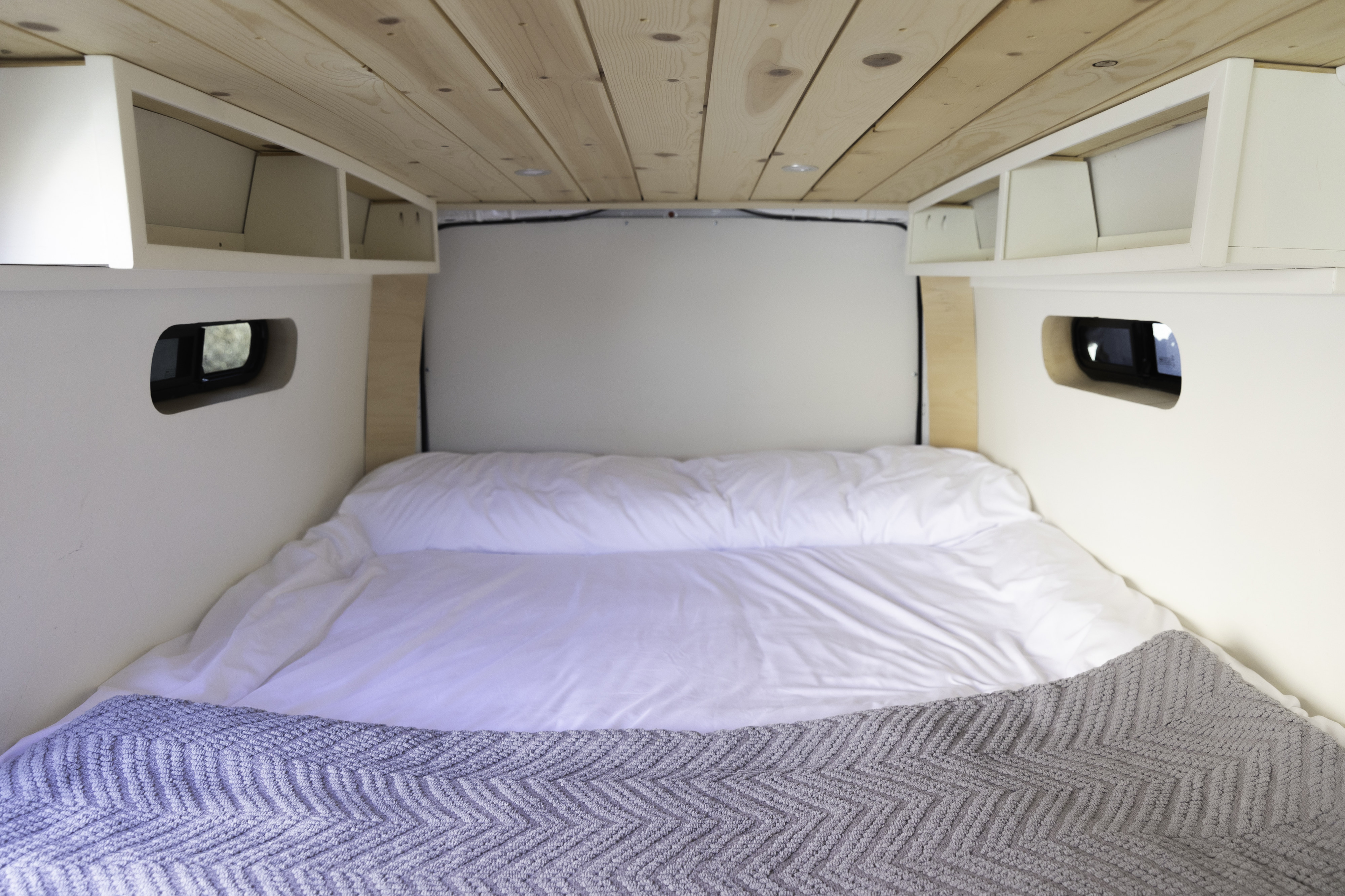 Serene RV rental sleeping area featuring a plush bed, natural wood ceiling, and practical overhead storage compartments.. Mercedes-Benz Metris 2021