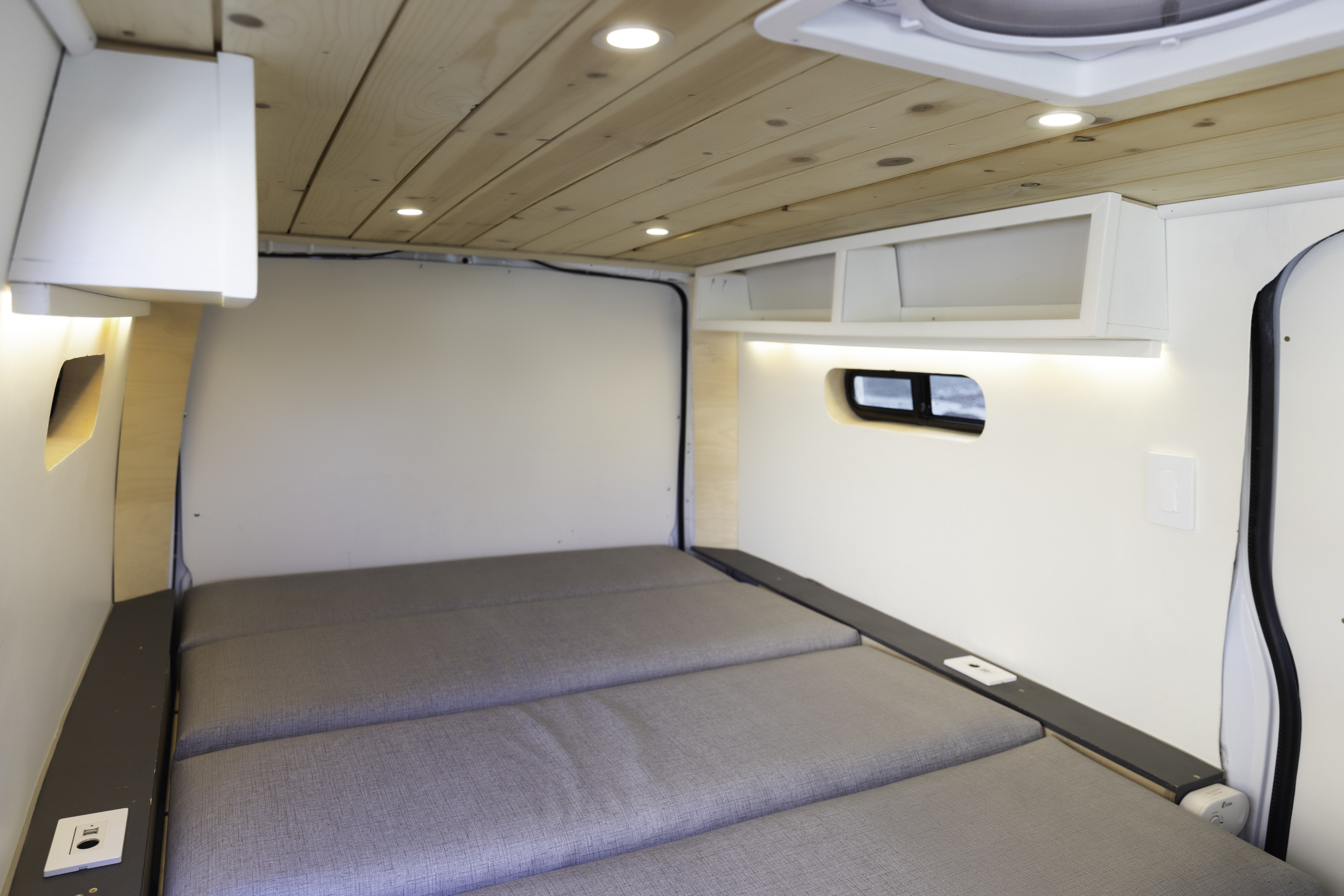 Cozy RV rental interior with a comfortable grey bed, wooden ceiling, and bright LED lighting, perfect for van life adventures.. Mercedes-Benz Metris 2021