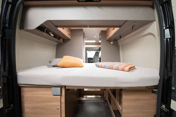 Inside an RV rental, a comfy bed and storage are visible in the rear. View extends through the camper van to the front cabin.. Dethleffs Globetrail 600DB 2024