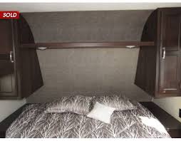 Inside an RV rental, this bedroom features dark wood cabinets flanking a recessed headboard area above a bed with a patterned comforter.. Jayco Jay Flight SLX 2020