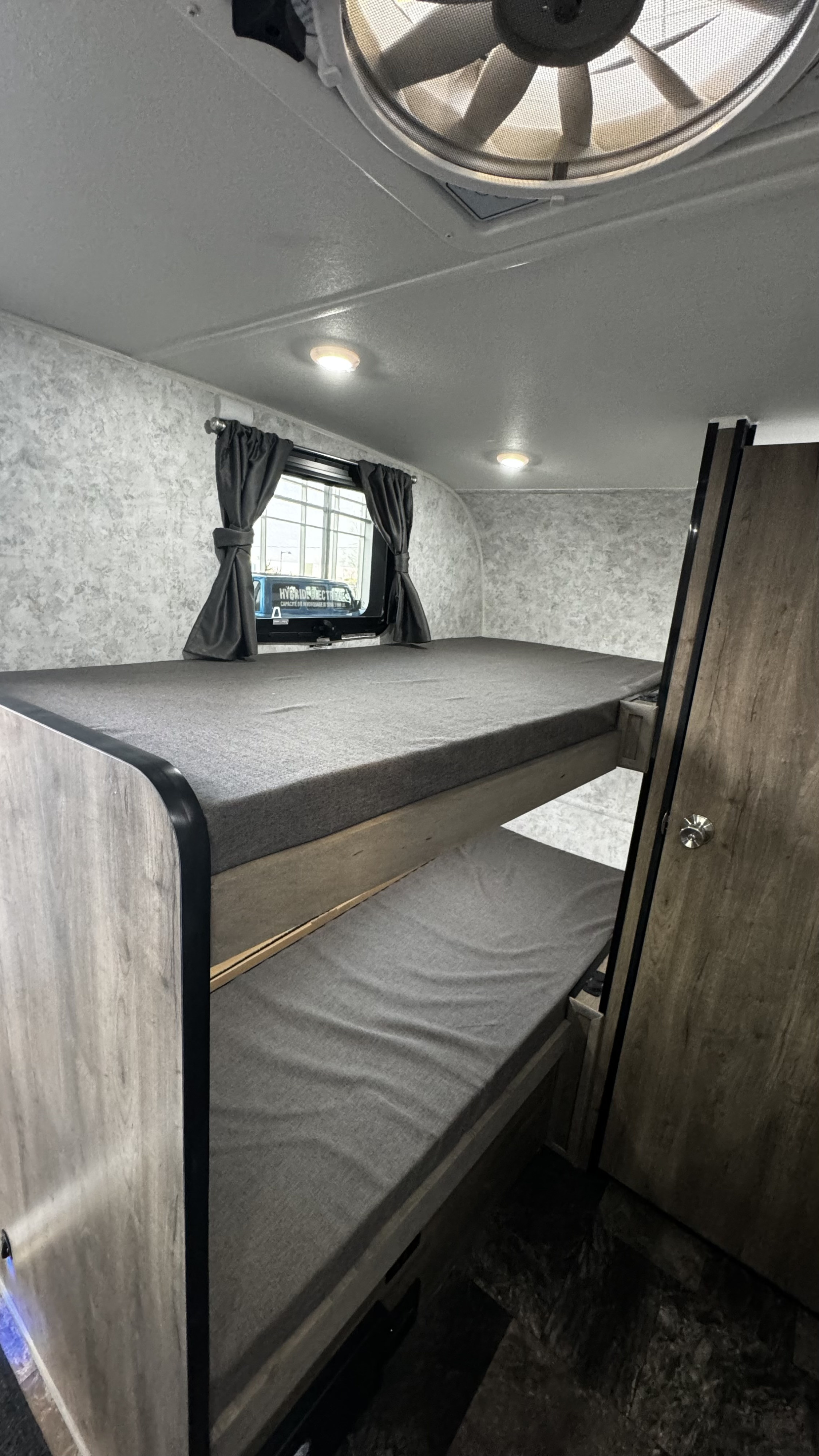 Cozy RV rental interior with comfortable bunk beds featuring grey mattresses and wood-look frames, ideal for family travel.. Prolite Profil 2024