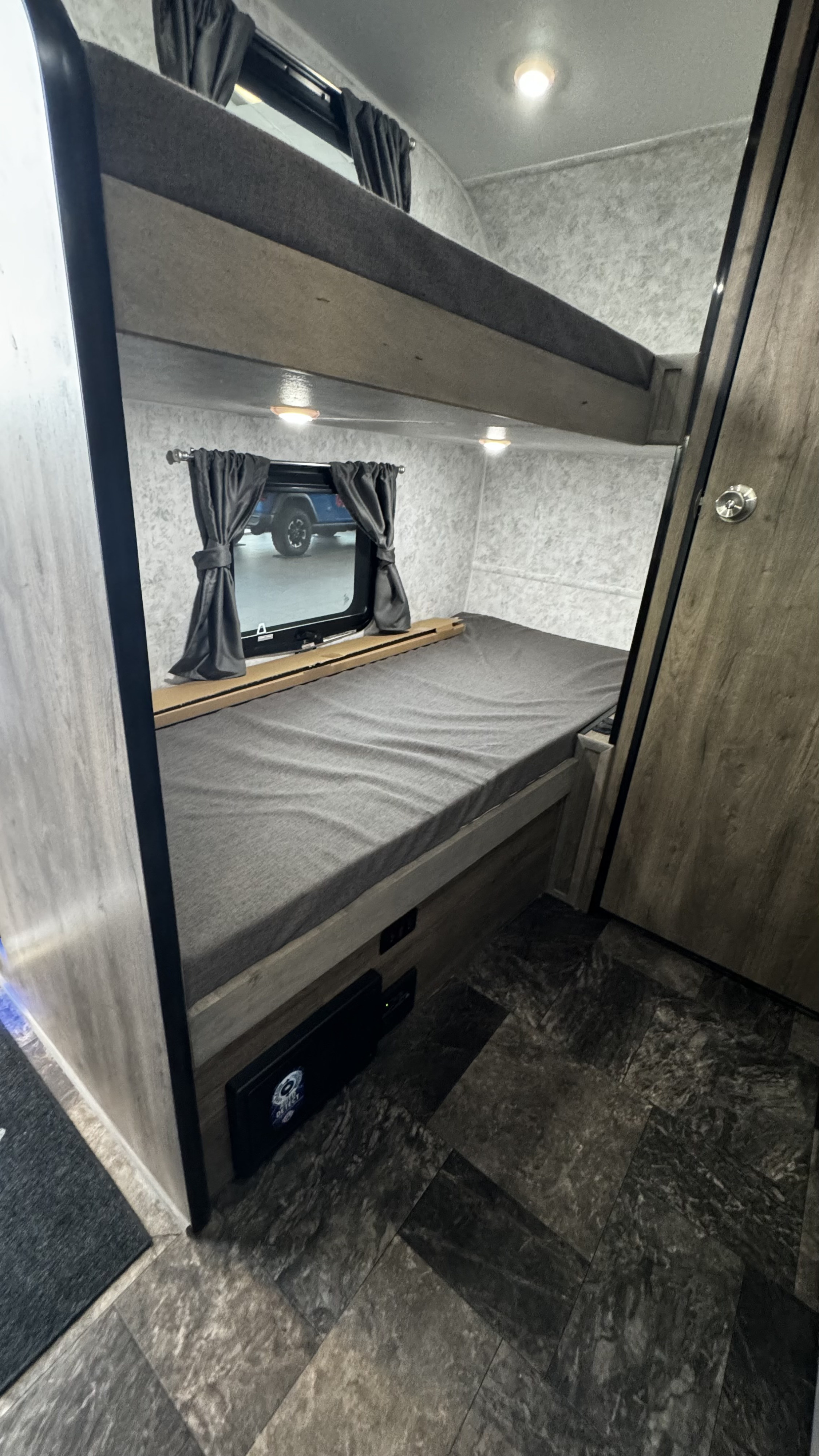 Inside this RV rental: a bunk bed with a window view of a blue vehicle outside, dark patterned flooring, and built-in amenities.. Prolite Profil 2024