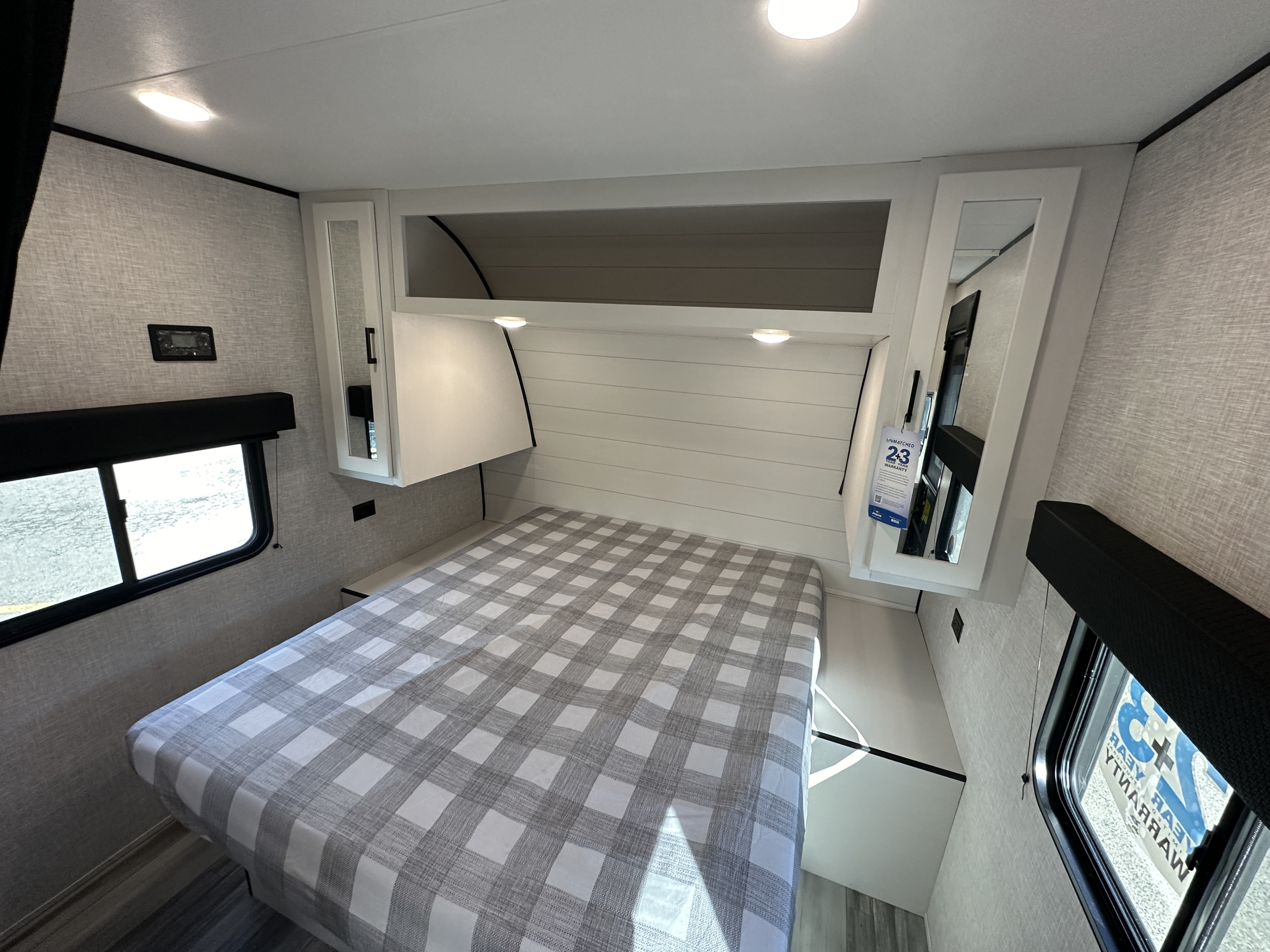 RV rental bedroom: a cozy space featuring a bed with a gray and white checkered comforter, overhead storage, and windows.. Jayco Jay Flight 2024