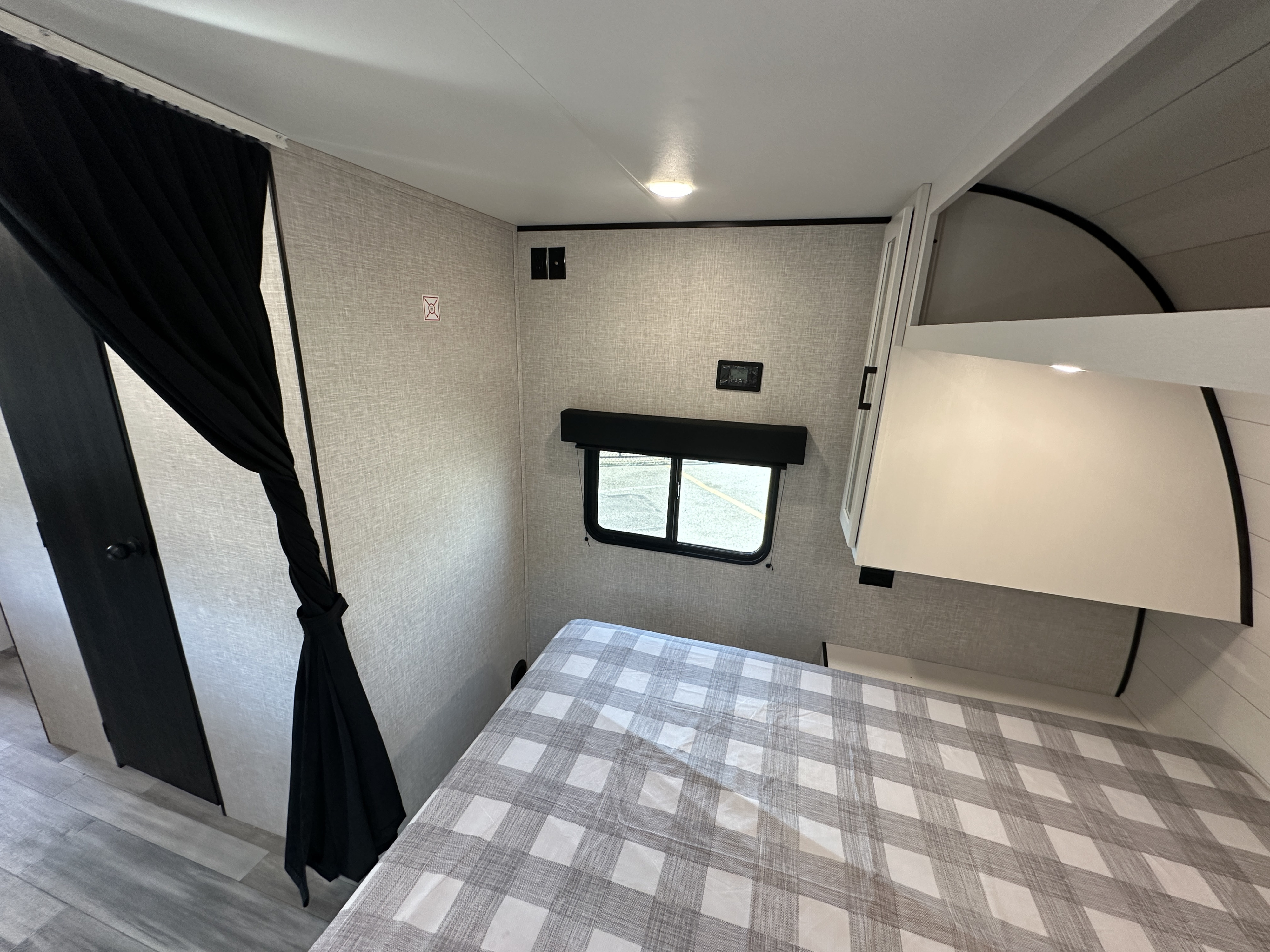 Inside a modern RV rental: a cozy bedroom with a plaid comforter, window, and clean design. Ideal for travelers.. Jayco Jay Flight 2024