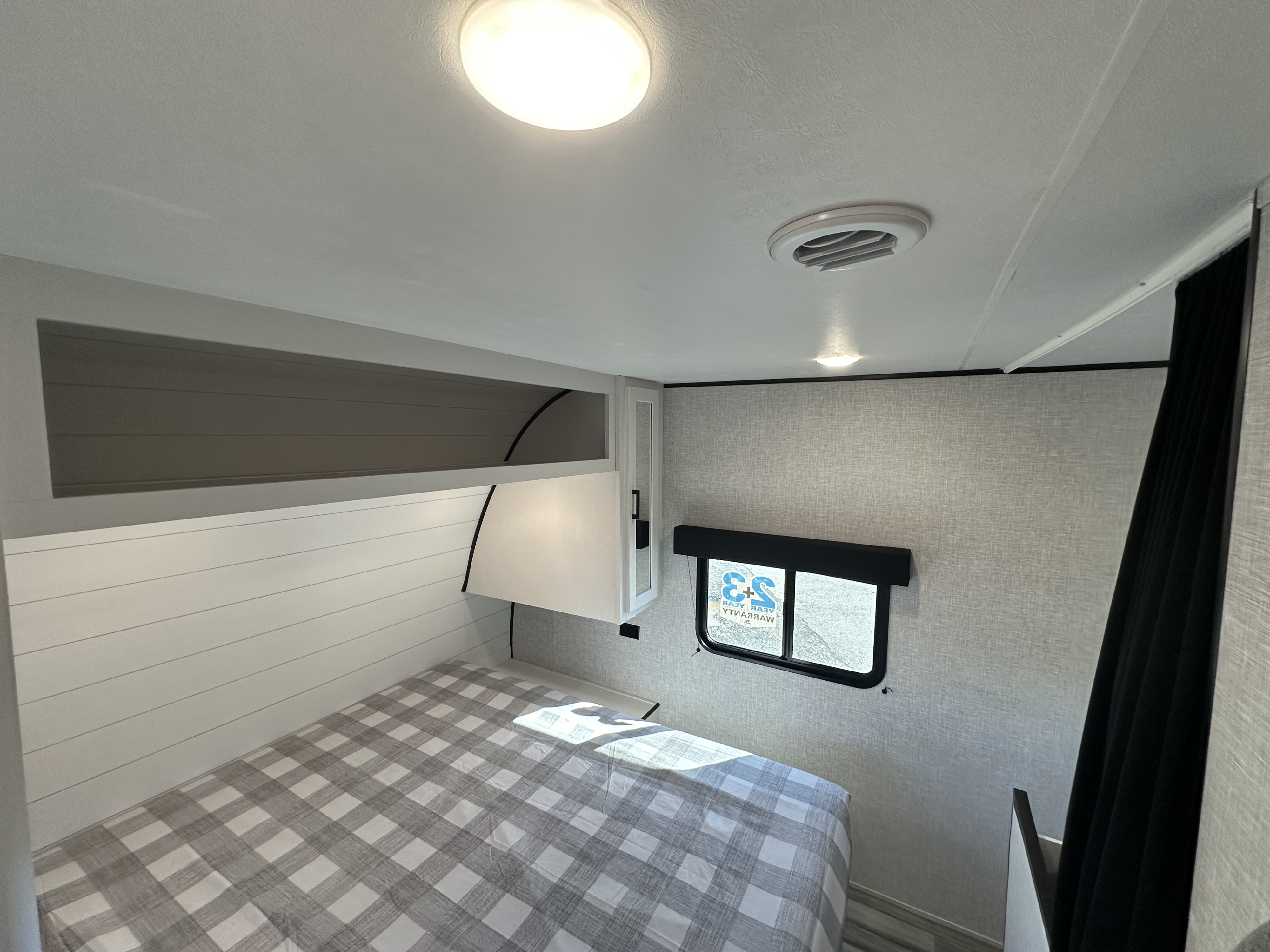 Modern RV rental bedroom featuring a comfy bed, ceiling light, AC vent, window, and ample overhead storage.. Jayco Jay Flight 2024