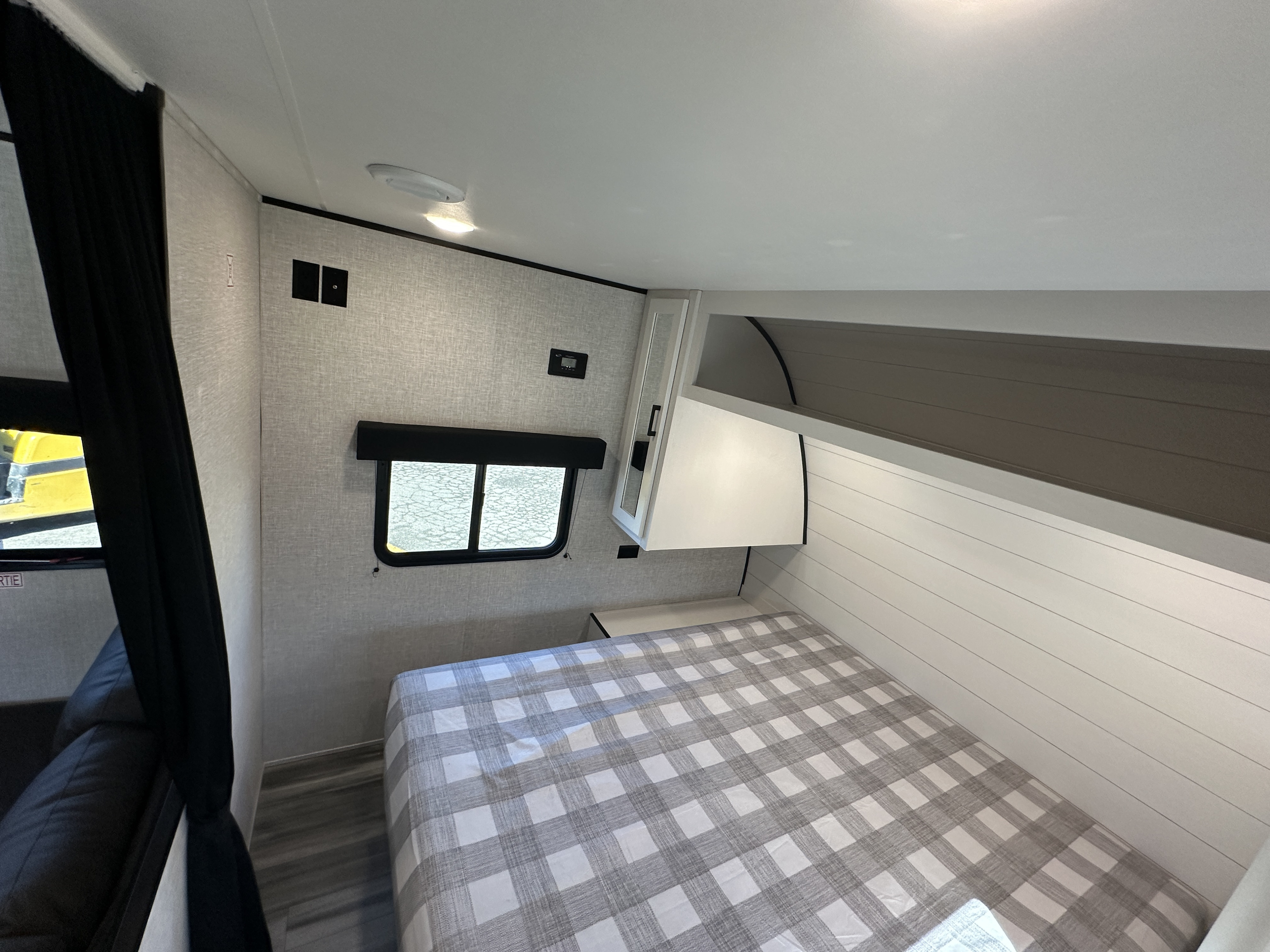 Compact RV rental bedroom with gray checkered bed, shiplap wall, overhead storage, and windows for natural light.. Jayco Jay Flight 2024