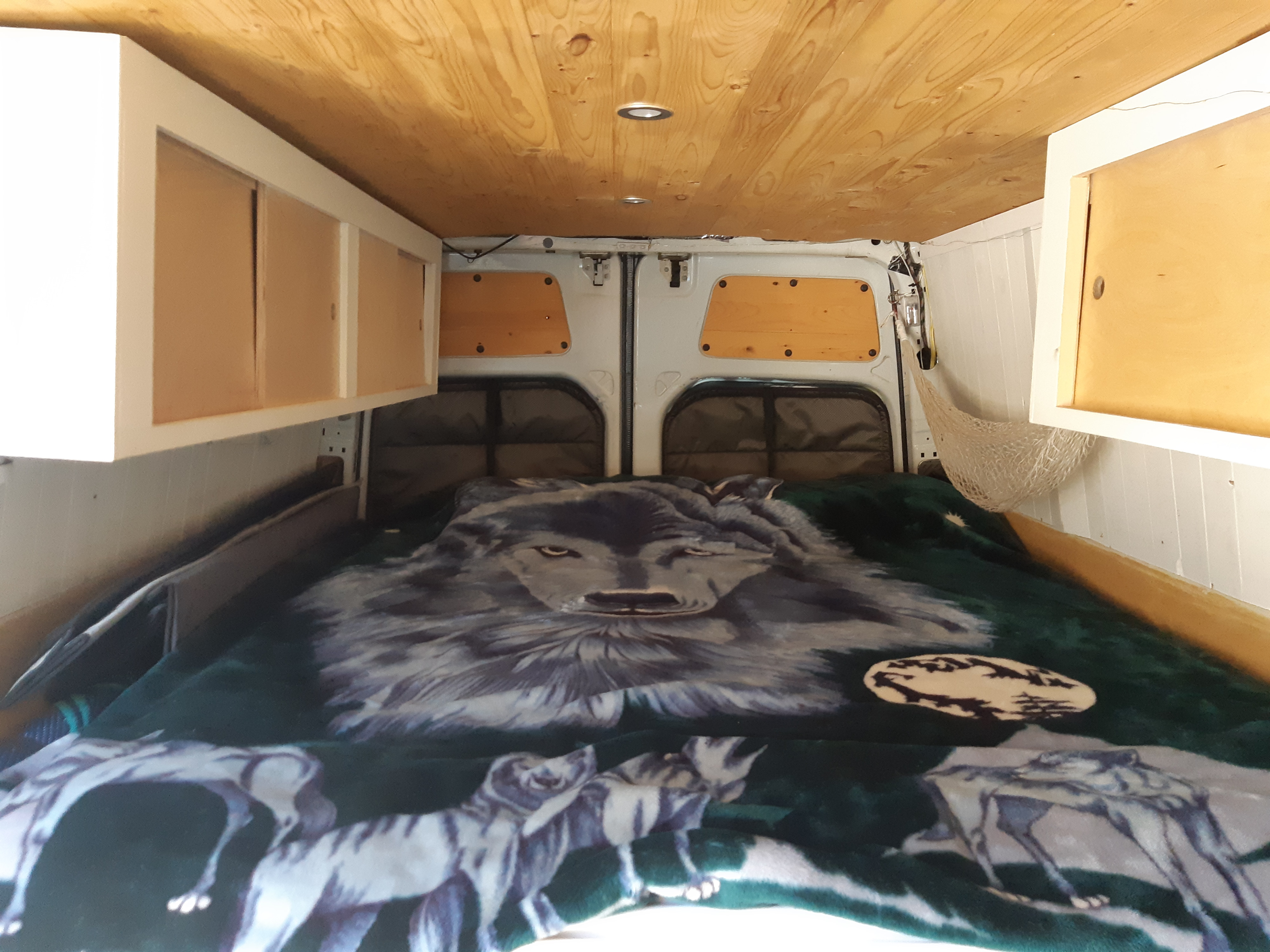 View inside an RV rental: custom wood ceiling, overhead cabinets, and a bed with a detailed wolf blanket.. Dodge Sprinter 2007