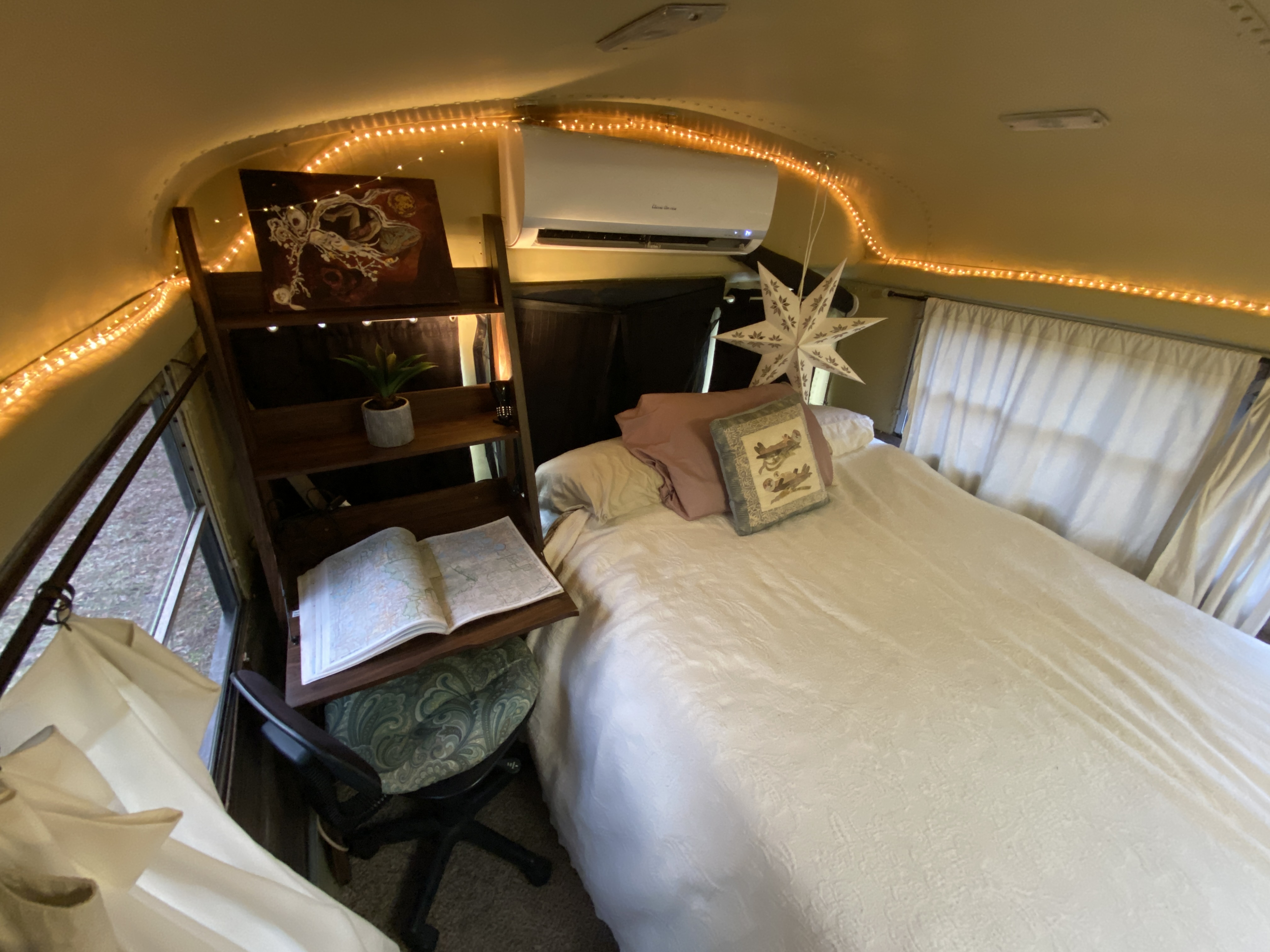 Cozy RV rental bedroom featuring soft lighting, an AC unit, and a small desk/bedside area with a map book.. International 510A 1996