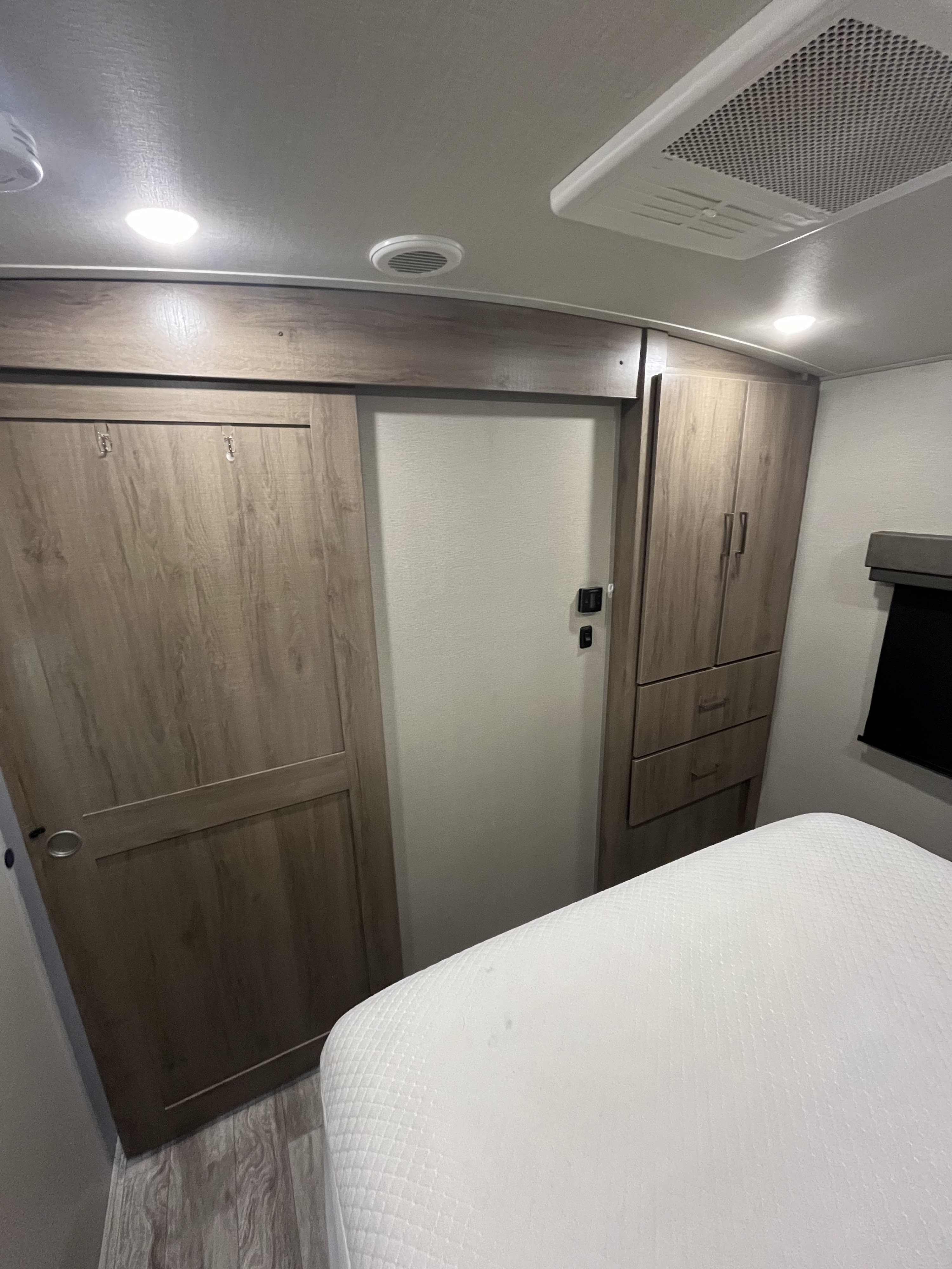 Compact RV rental bedroom showing a bed, wooden sliding closet, and built-in storage cabinet.. Grand Design Imagine 2023