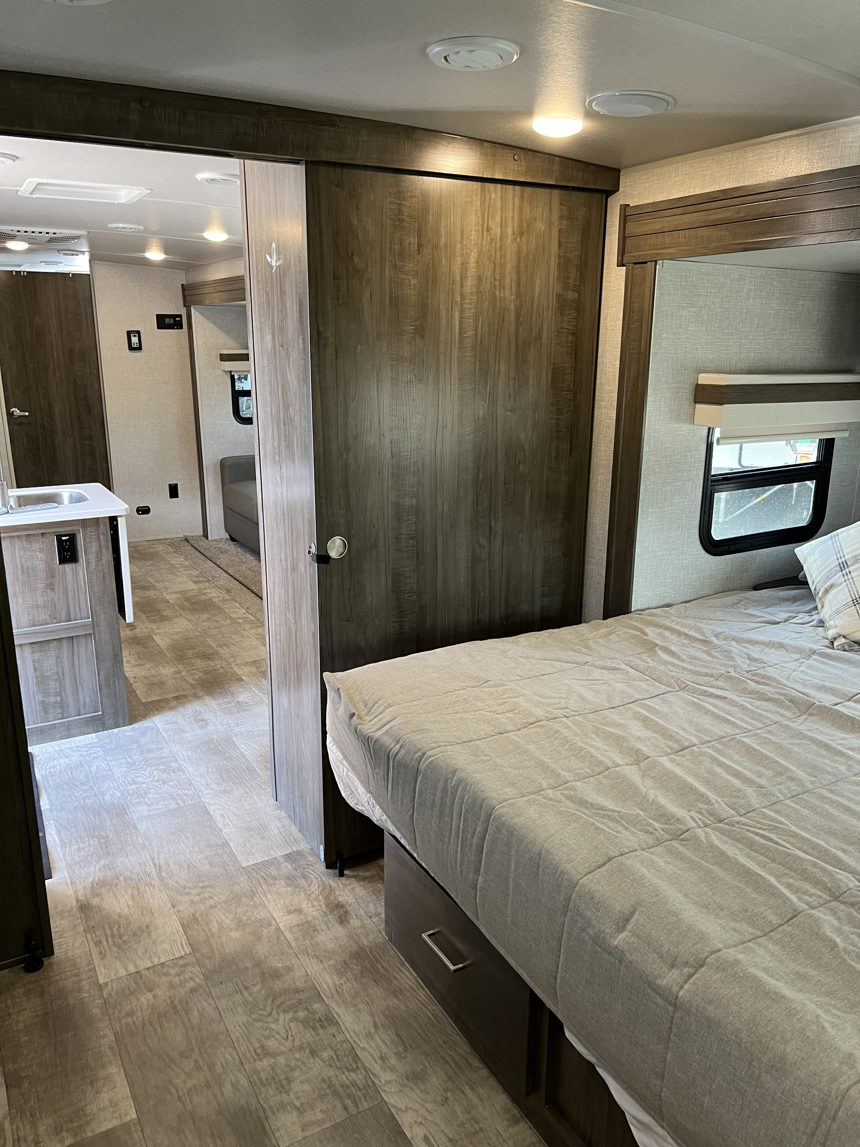Inside an RV rental: a bedroom with a neatly made bed and built-in storage, looking toward the kitchen/living area.. Forest River Rockwood Ultra Lite 2022