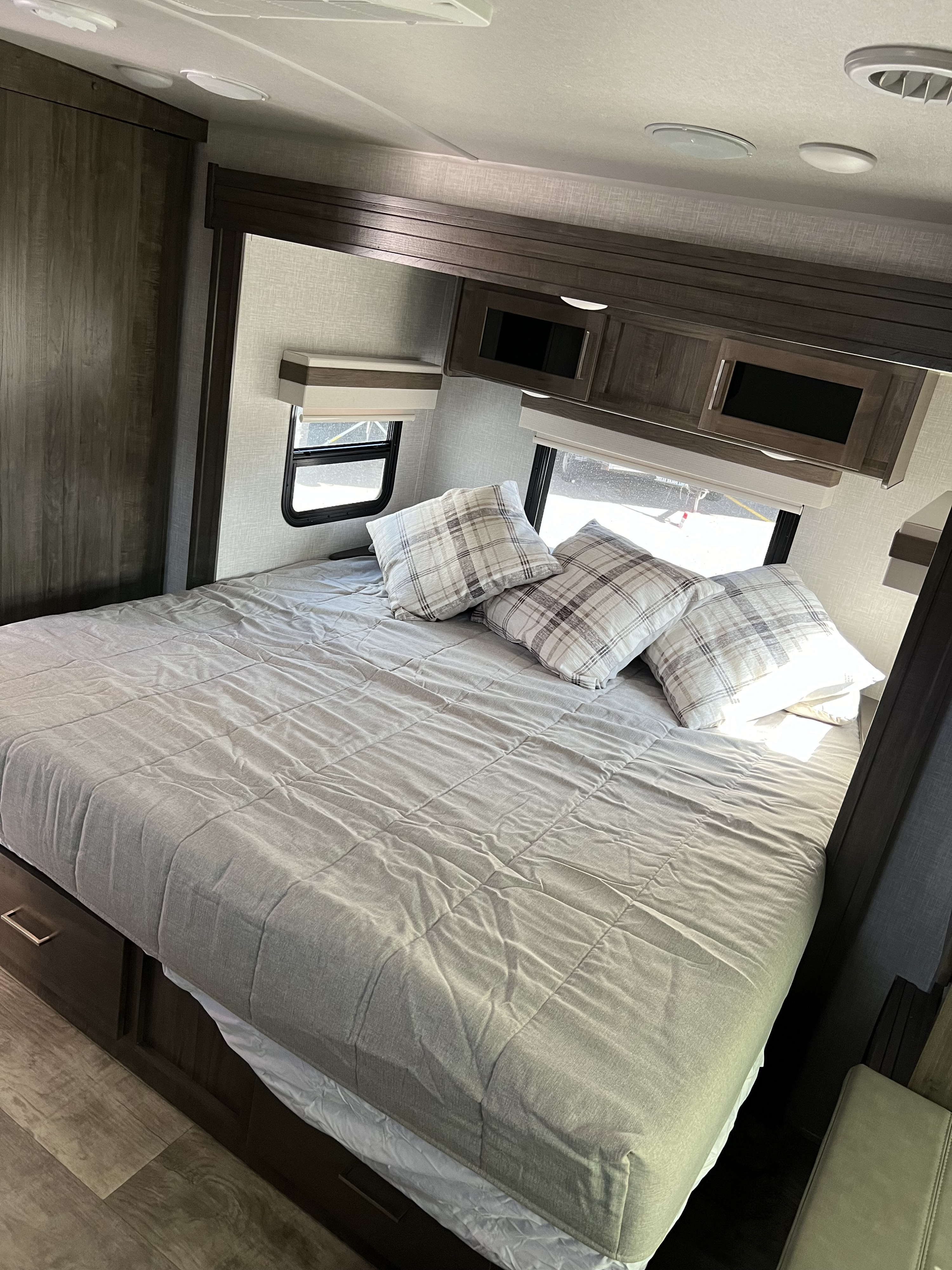Spacious RV rental bedroom with a cozy bed, plaid pillows, overhead storage, and windows. Ideal for travel comfort.. Forest River Rockwood Ultra Lite 2022