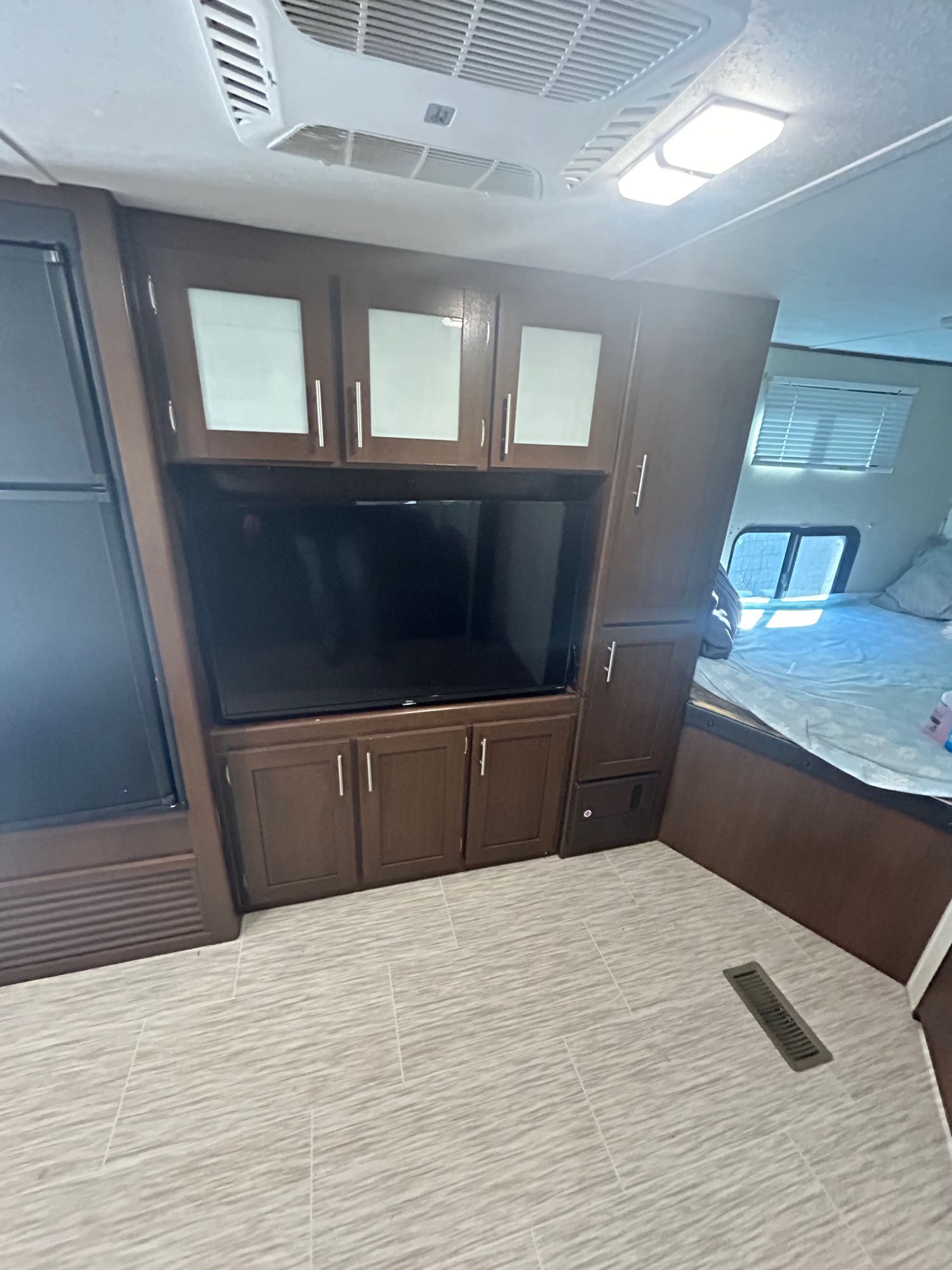 This RV rental's interior features a dark wood entertainment center with a TV, a fridge, and a sleeping area, all on a light tiled floor.. Avenger ATI 2018