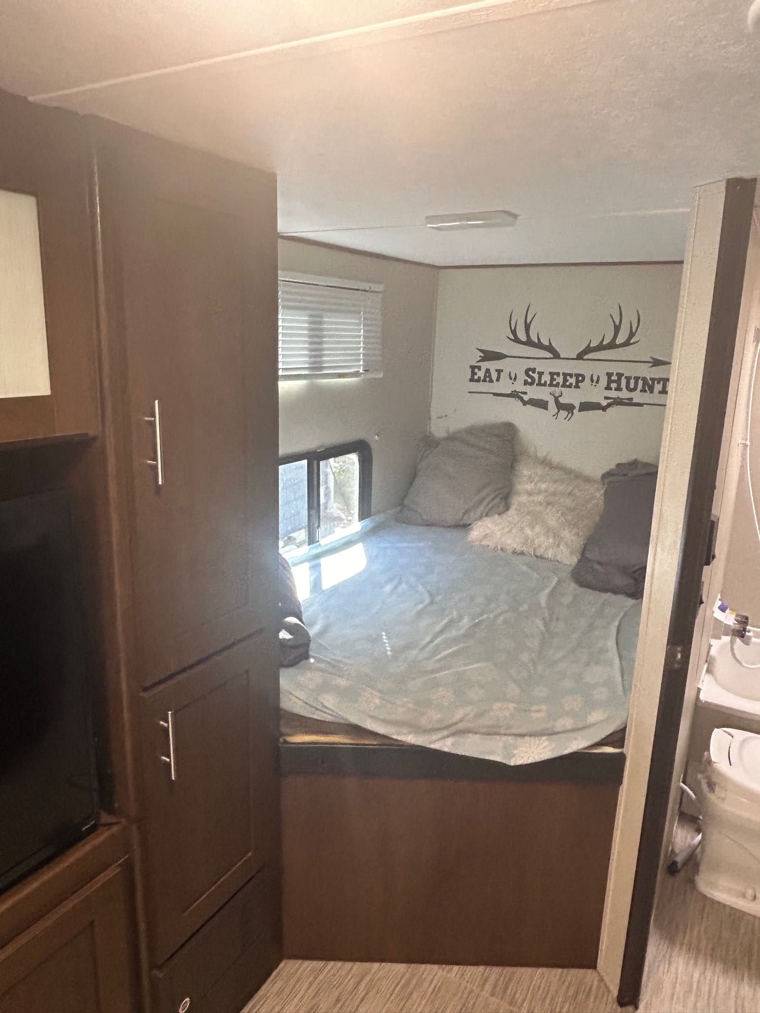 Cozy RV rental bedroom featuring a bed, hunting-themed wall decor, built-in cabinets, and glimpse of a compact bathroom.. Avenger ATI 2018