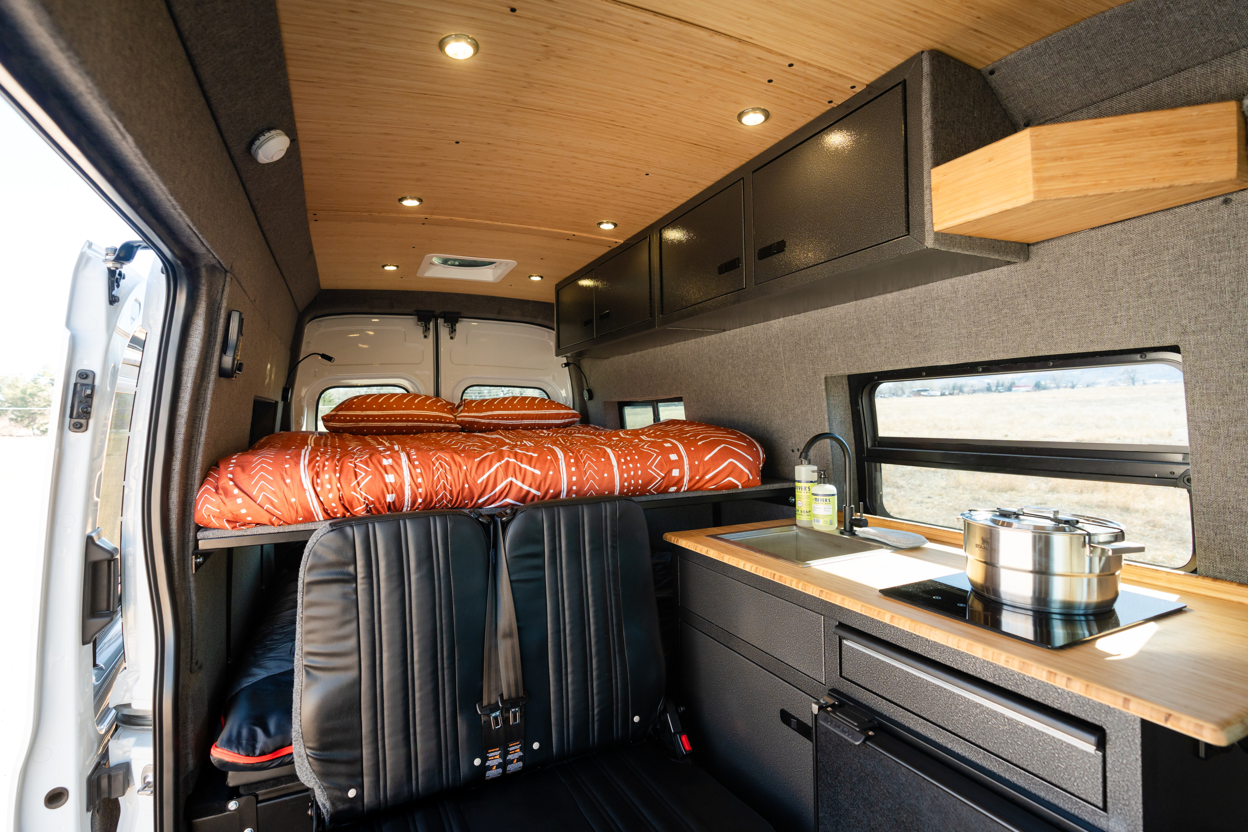 Cozy RV rental interior with a comfortable bed, compact kitchen, seating, and ample storage for mobile living.. Ford Transit 2024
