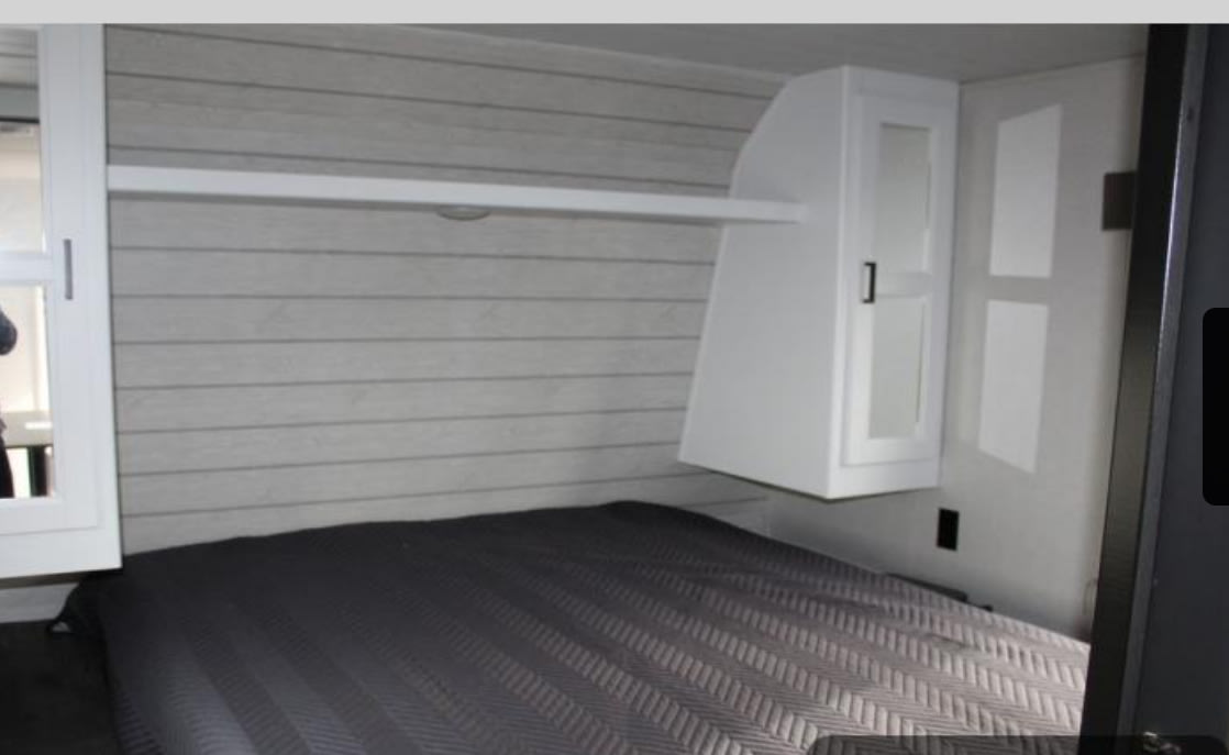 RV rental bedroom with gray horizontal paneling, a bed, overhead shelf, and white cabinet. Ideal for travel.. Keystone RV Hideout 2022