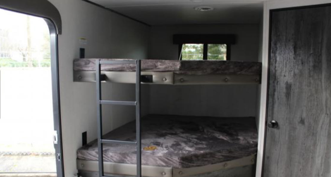 RV rental interior features comfortable bunk beds with a ladder, window view, and an interior door, ideal for families.. Keystone RV Hideout 2022