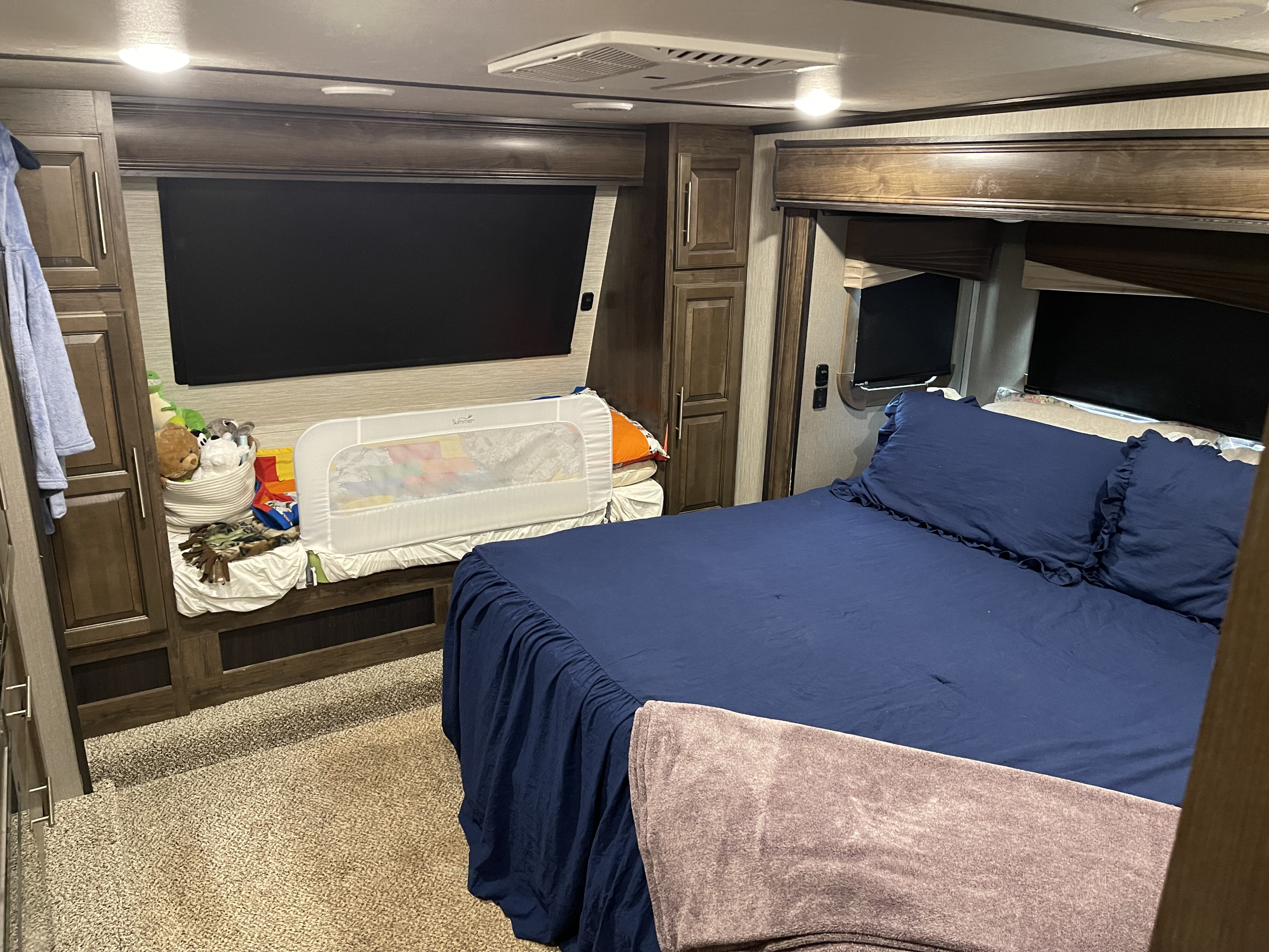 RV rental bedroom: dark blue bed with ruffled pillows, cozy blanket, child's bed rail, and built-in cabinetry.. Crossroads RV Cameo 2019