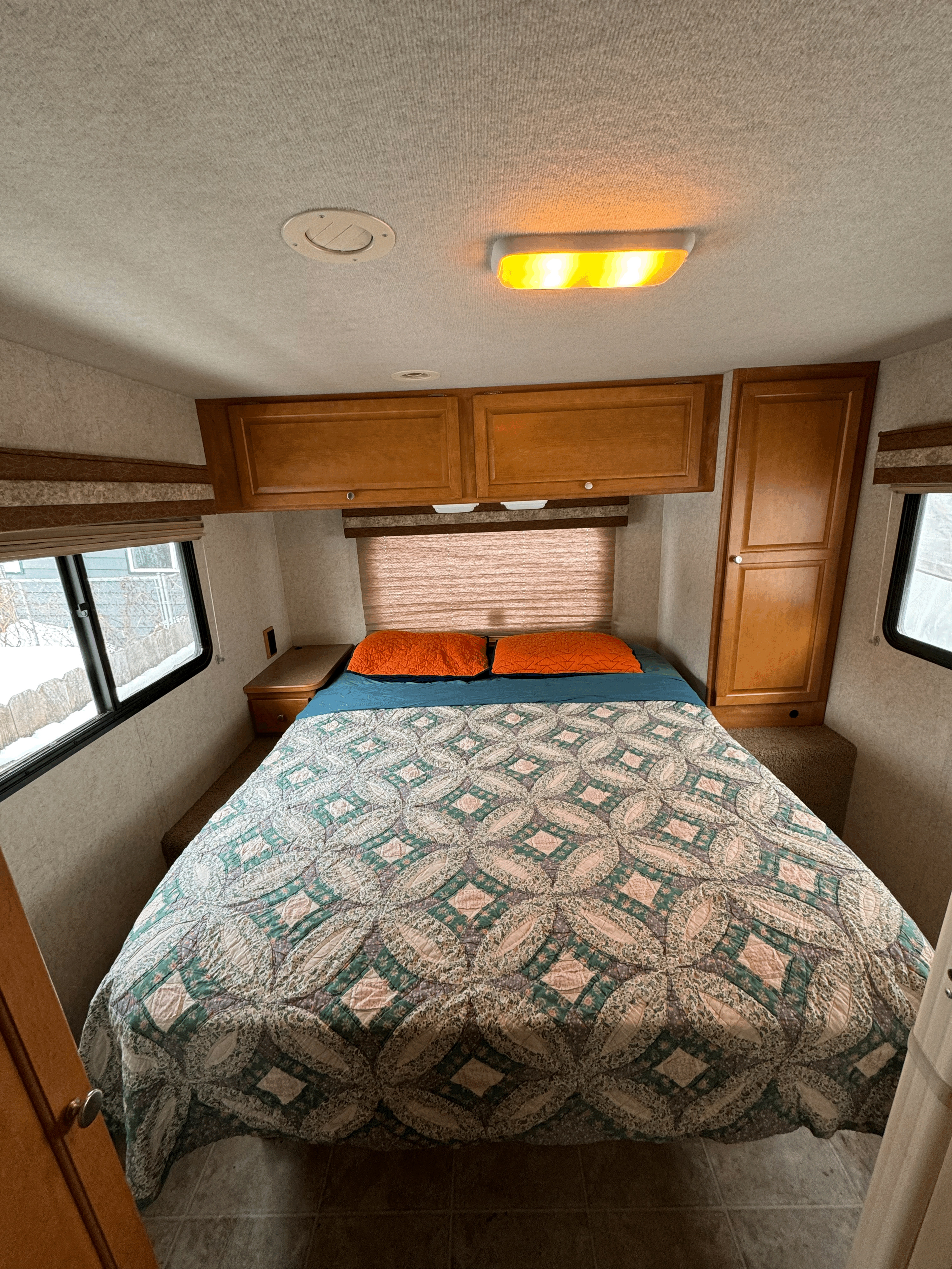 Cozy bedroom interior of an RV rental, featuring a patterned quilt, overhead cabinets, and windows. Perfect for travel comfort.. Winnebago Chalet 2009