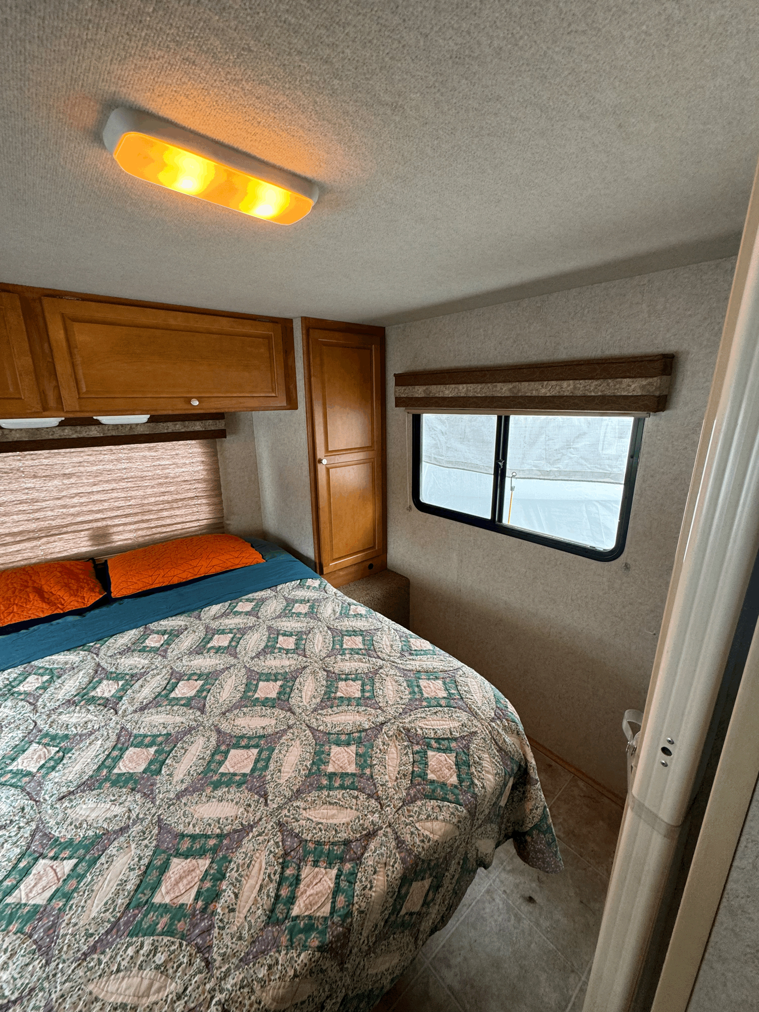 Relaxing RV rental bedroom featuring a patterned quilt on the bed, wood cabinets, and a window for comfortable travel.. Winnebago Chalet 2009