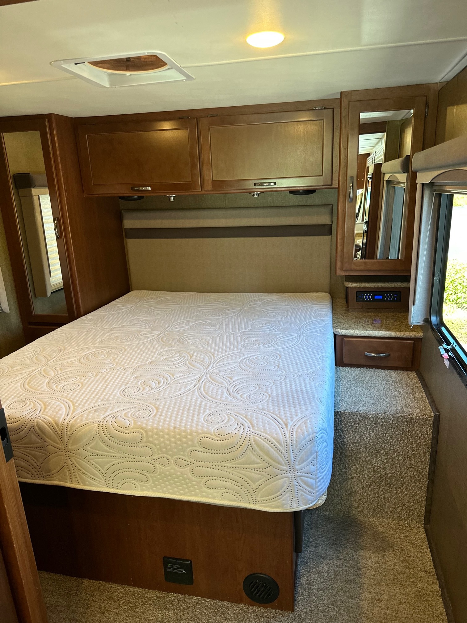 Cozy RV rental bedroom with a comfortable bed, overhead cabinets, and essential controls for your road trip comfort.. Thor Motor Coach A.C.E 2016