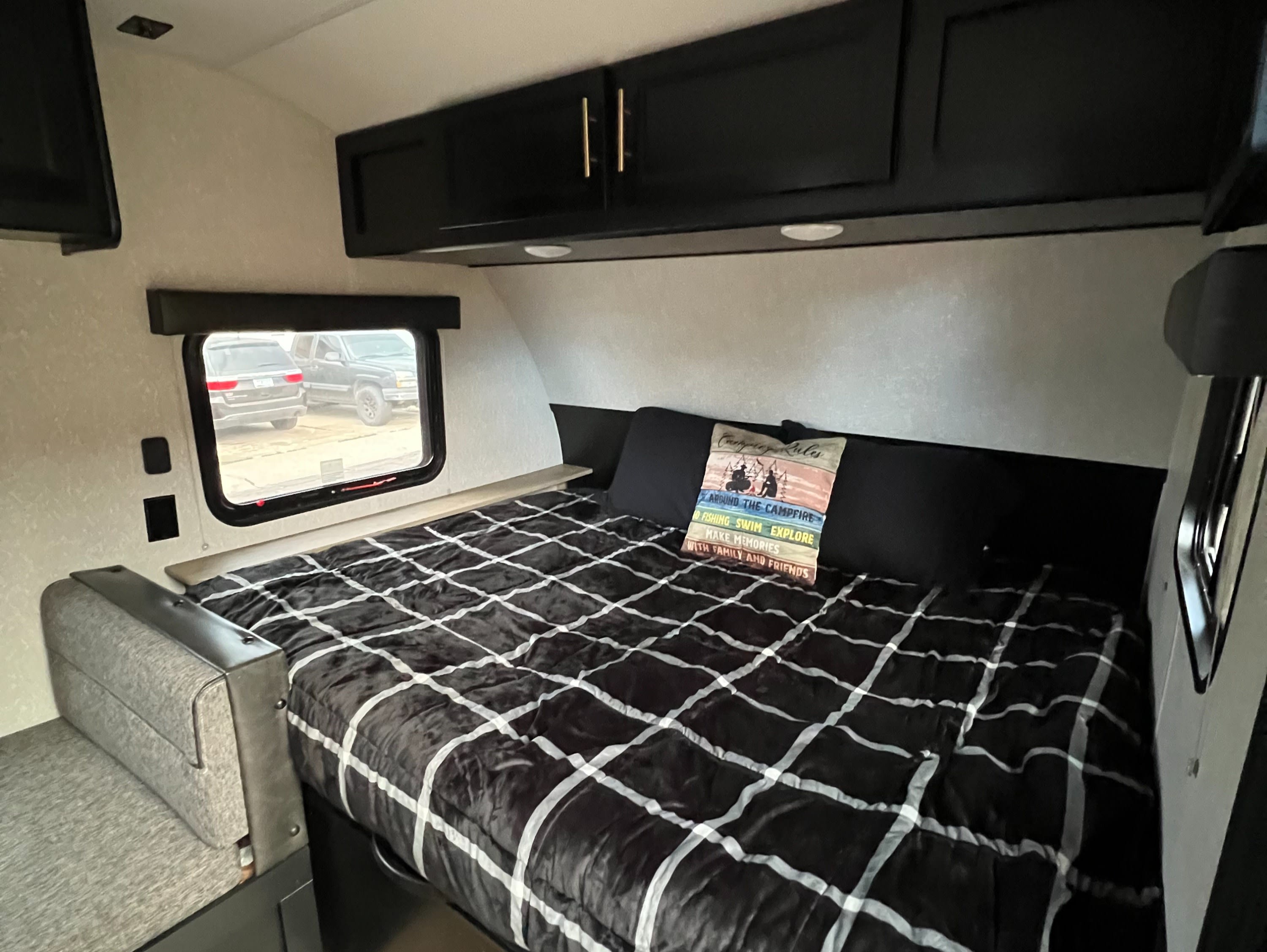 This cozy rv rental interior features a bed with a "Camping Rules" pillow, sleek black cabinets, and a bright window view.. Forest River Cherokee Wolf Pup 2022