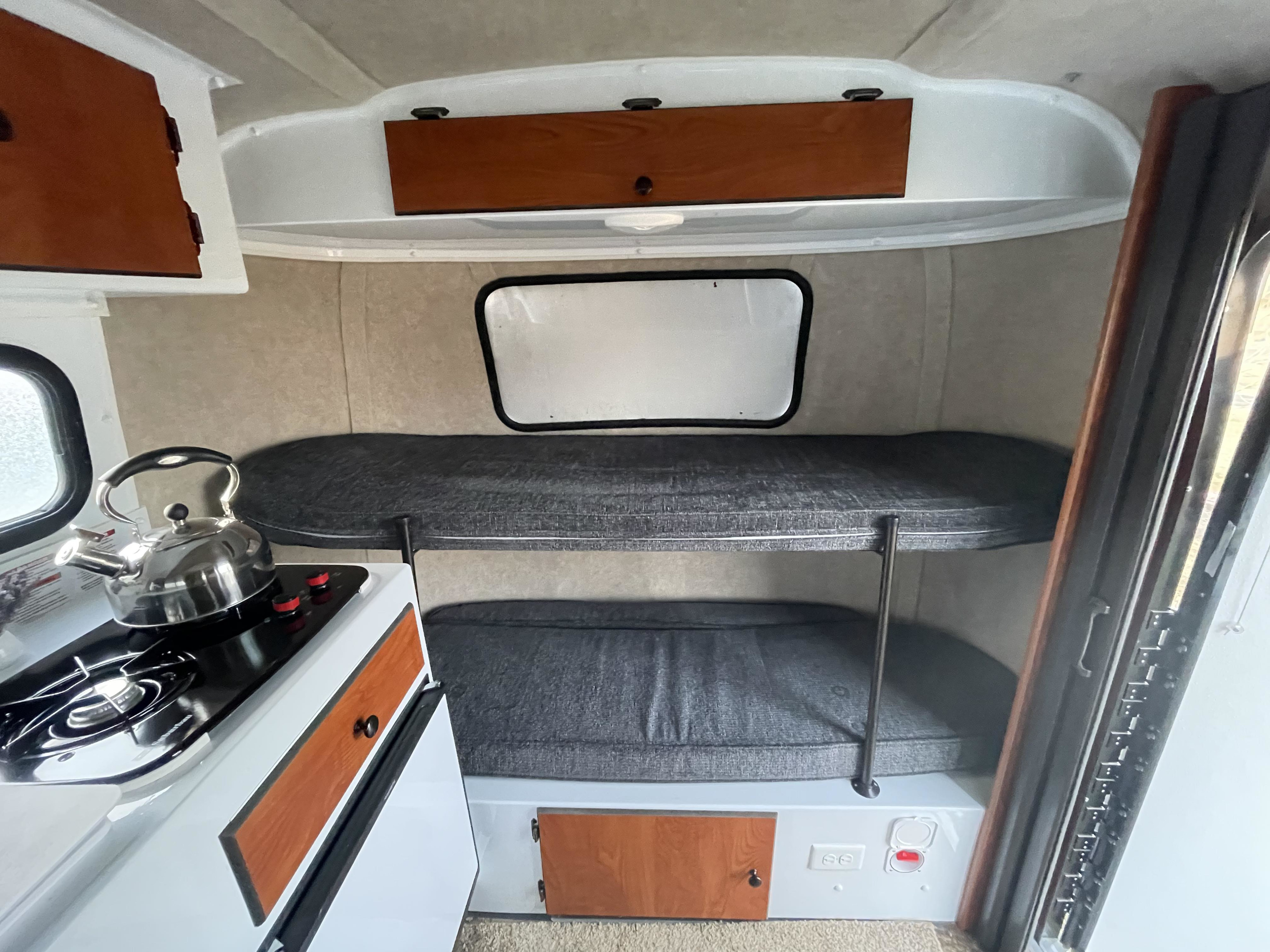 Cozy RV rental interior with a compact kitchenette, two-level bunk beds, and overhead storage, ideal for travel adventures.. Scamp Scamp Trailer 2021
