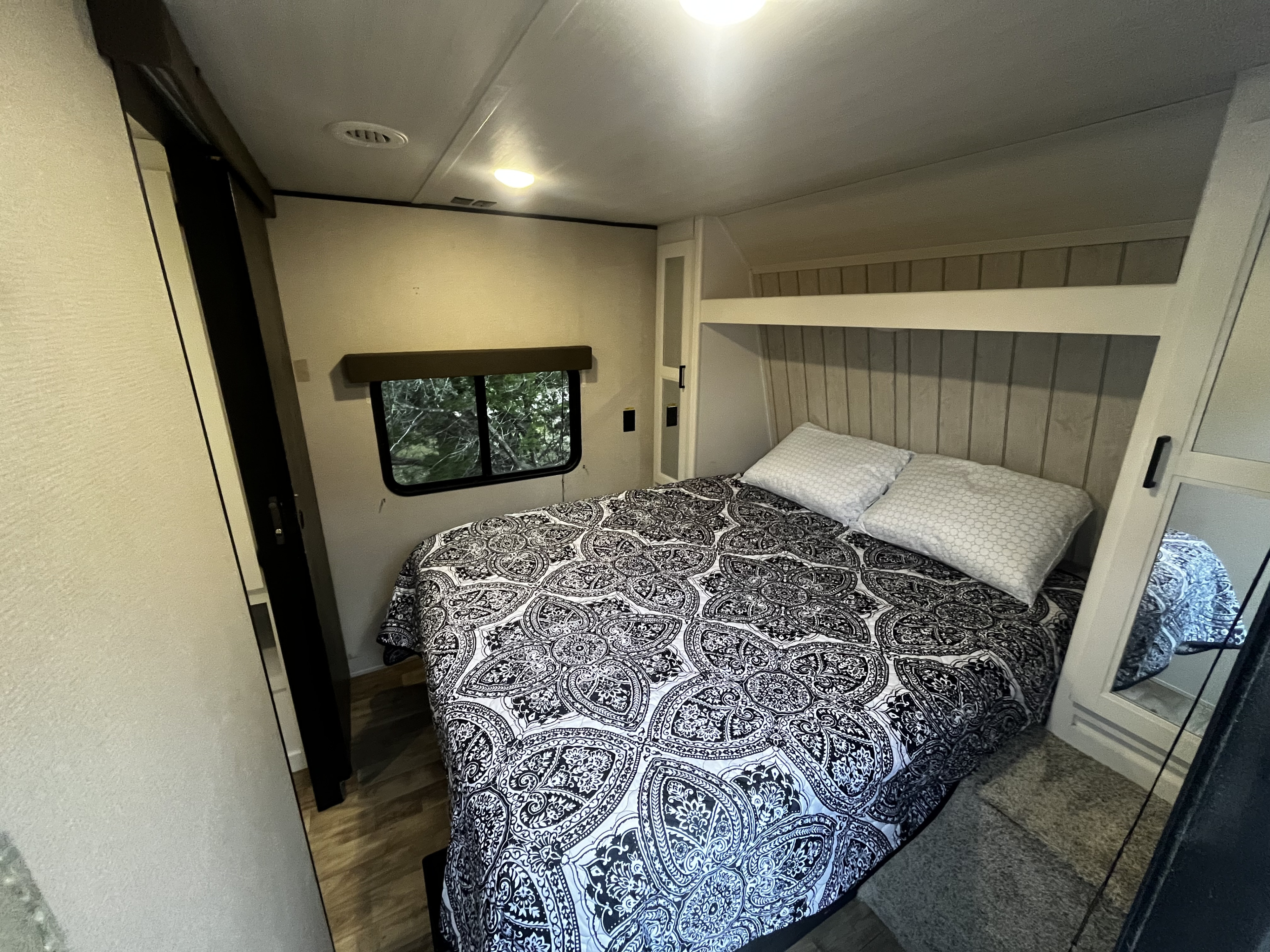 Cozy rv rental bedroom with a patterned bed, two pillows, built-in storage, and a window offering a view of trees.. Keystone RV Hideout 2022