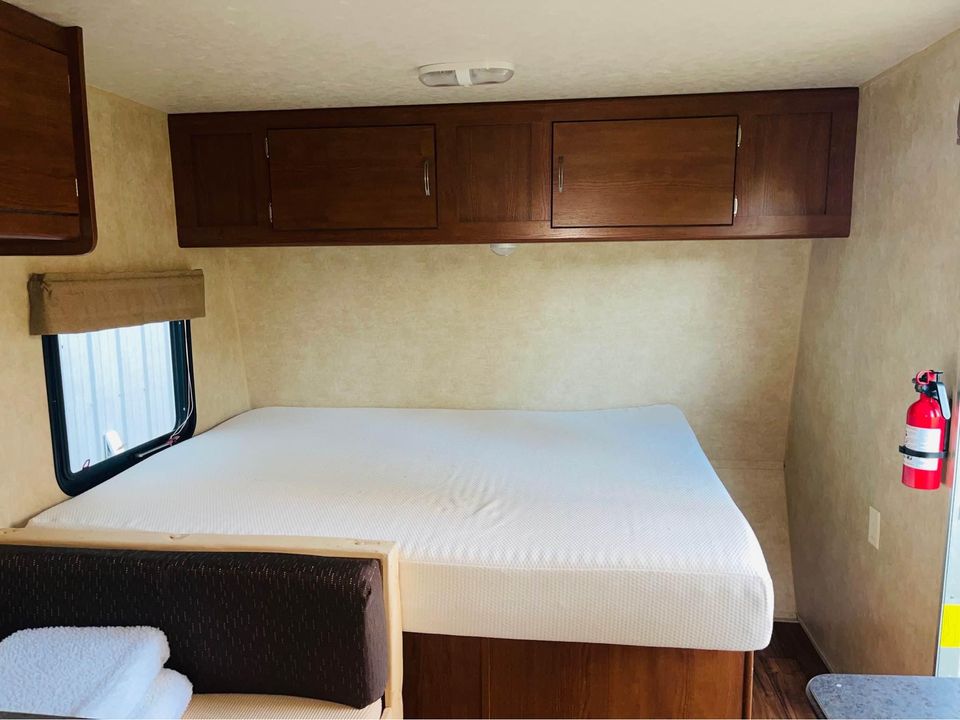 Spacious RV rental interior featuring a large bed, overhead cabinets, window, and fire extinguisher. Ideal for comfortable travels.. Forest River Wildwood X-Lite FS 2015