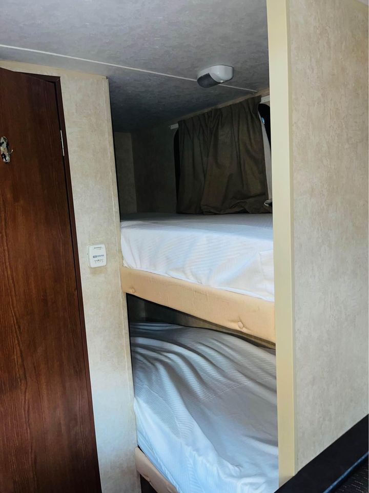 RV rental bunk bed setup: a clean, compact sleeping area with fresh white sheets, perfect for family trips.. Forest River Wildwood X-Lite FS 2015