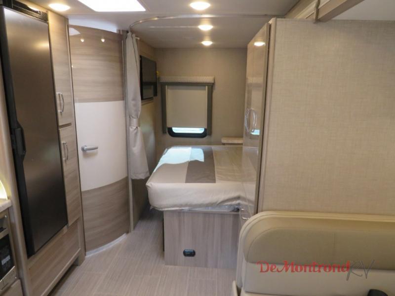 RV rental interior showing a cozy bedroom area with bed, fridge, cabinetry, and window.. Thor Tiburon 2023