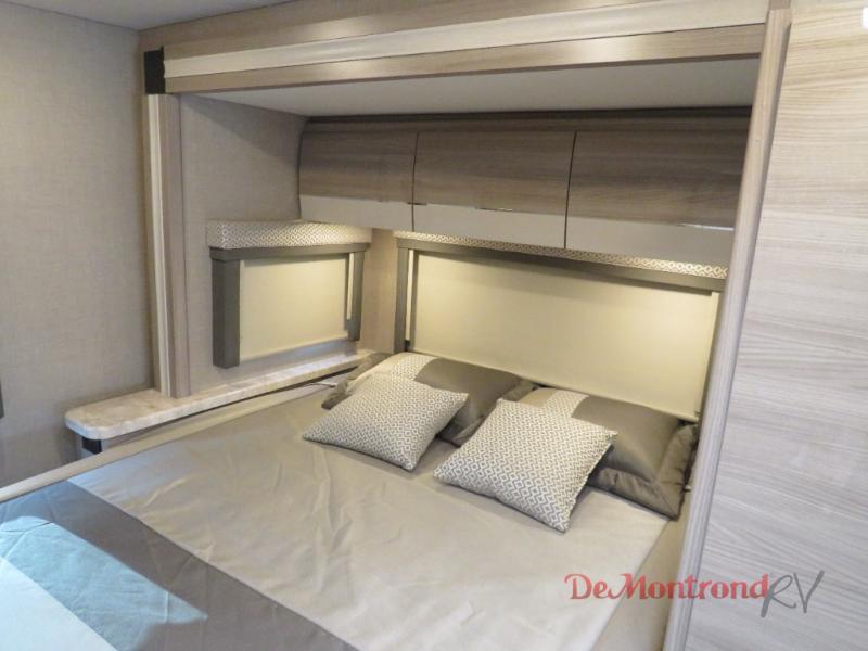This inviting RV rental bedroom offers a comfortable bed, overhead cabinets for storage, and window shades, ideal for travel.. Thor Tiburon 2023