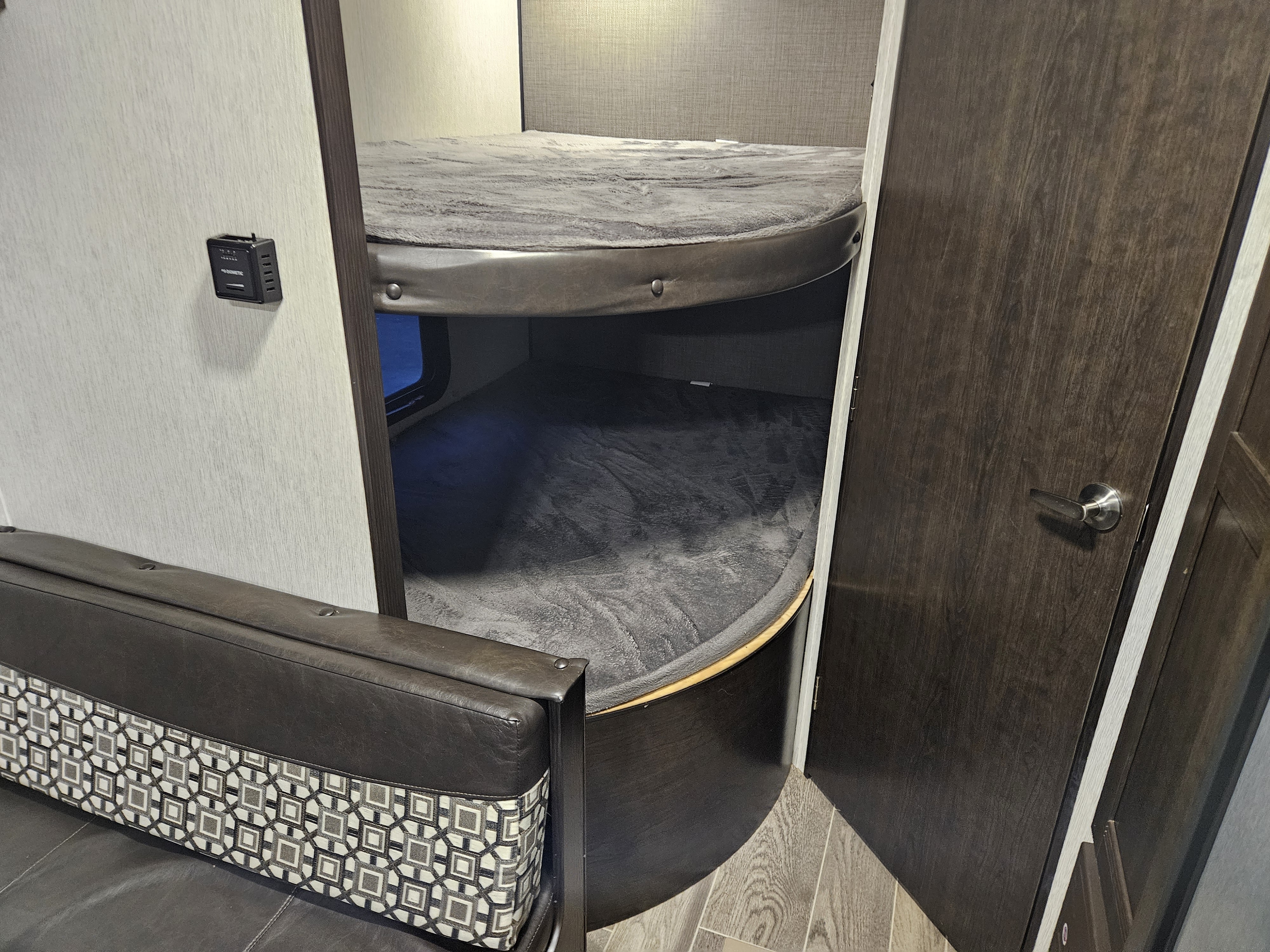 RV rental interior showcasing cozy bunk beds with soft gray mattresses and a stylish patterned sofa.. Heartland RVs Trail Runner SLE 2019