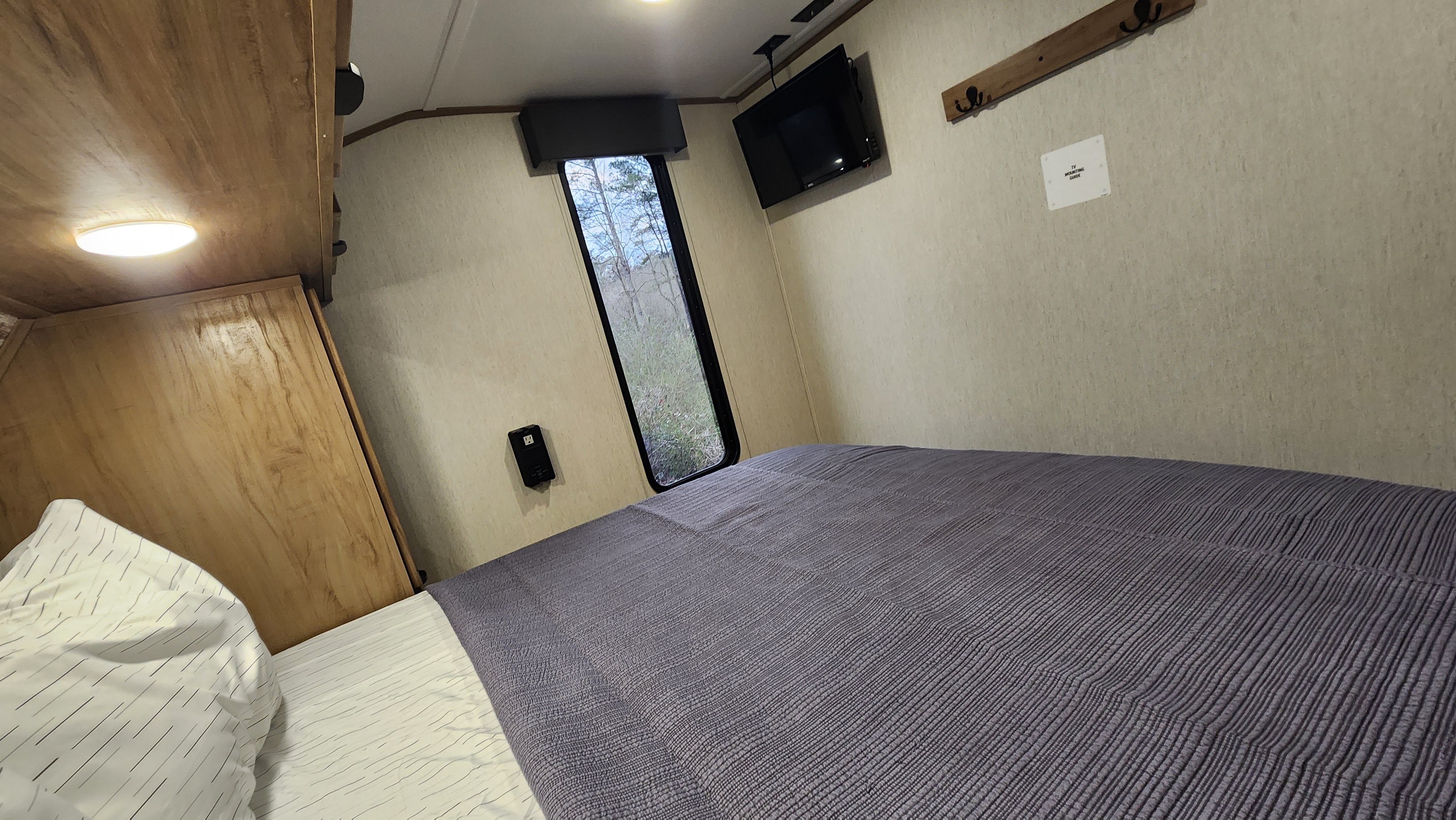 Comfortable RV rental bedroom featuring a cozy bed, window view, and mounted TV for your travels.. Forest River 22sw-l 2024