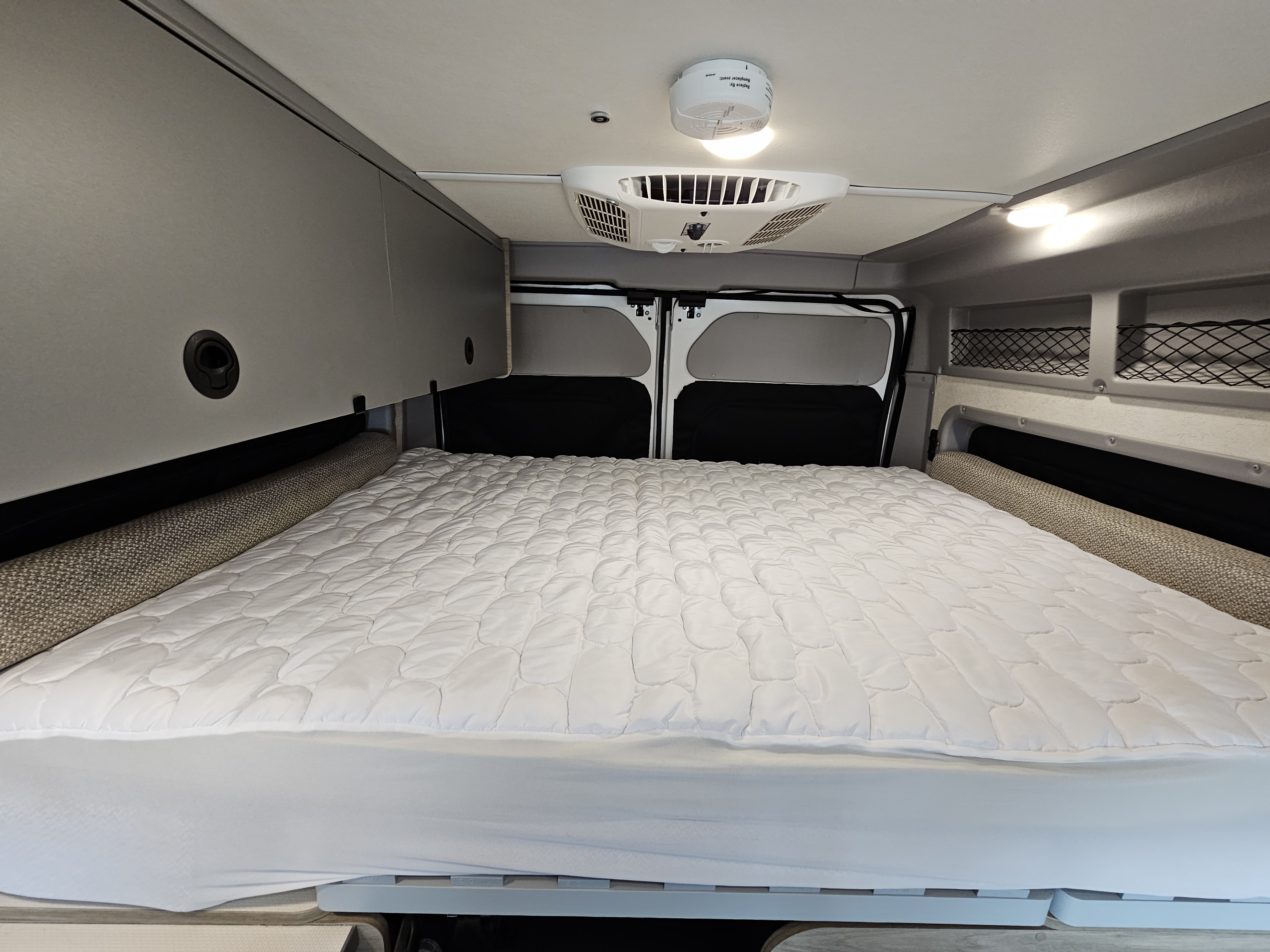 Cozy rv rental interior featuring a comfortable bed with a white mattress, overhead storage, and ceiling mounted AC unit.. Winnebago Solis 2022
