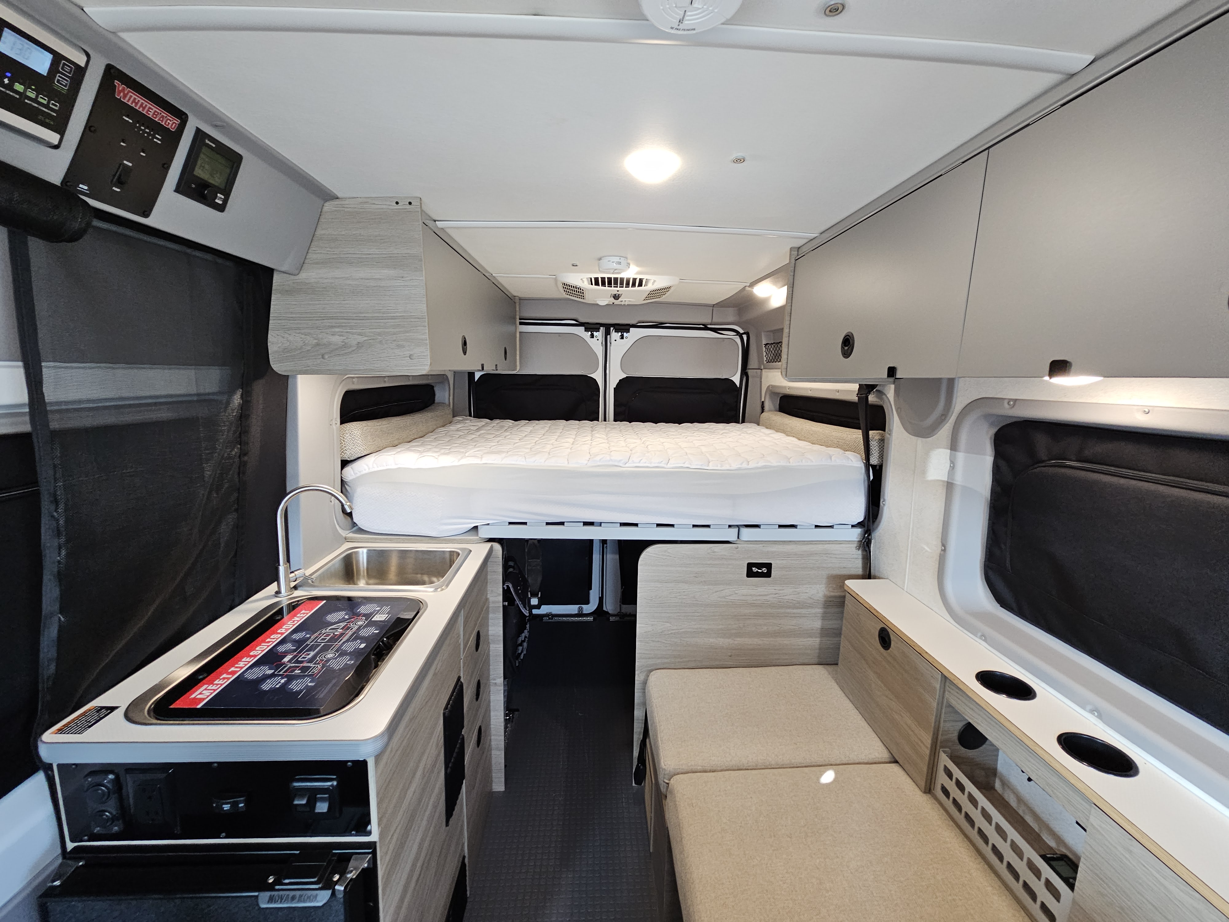 Inside this modern RV rental: a comfy bed, functional kitchenette, and lounge seating, perfect for road trips.. Winnebago Solis 2022