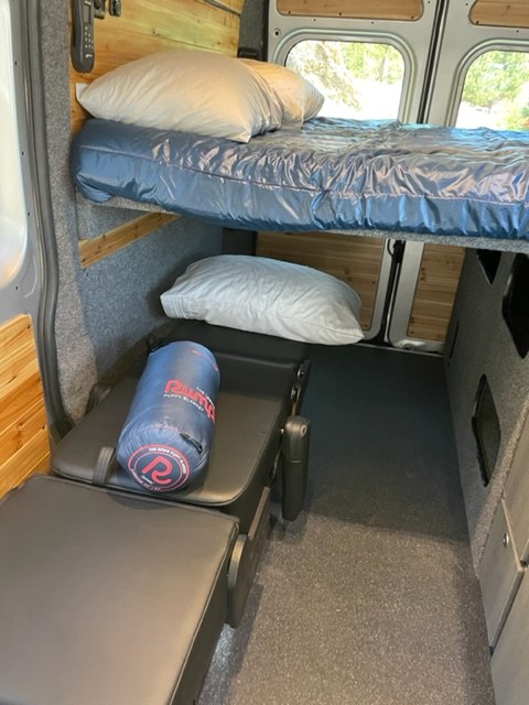 Cozy RV rental camper van interior featuring an upper bunk bed and a lower cushioned sleeping area.. RAM Promaster ALPINE X Edition OA16 2021