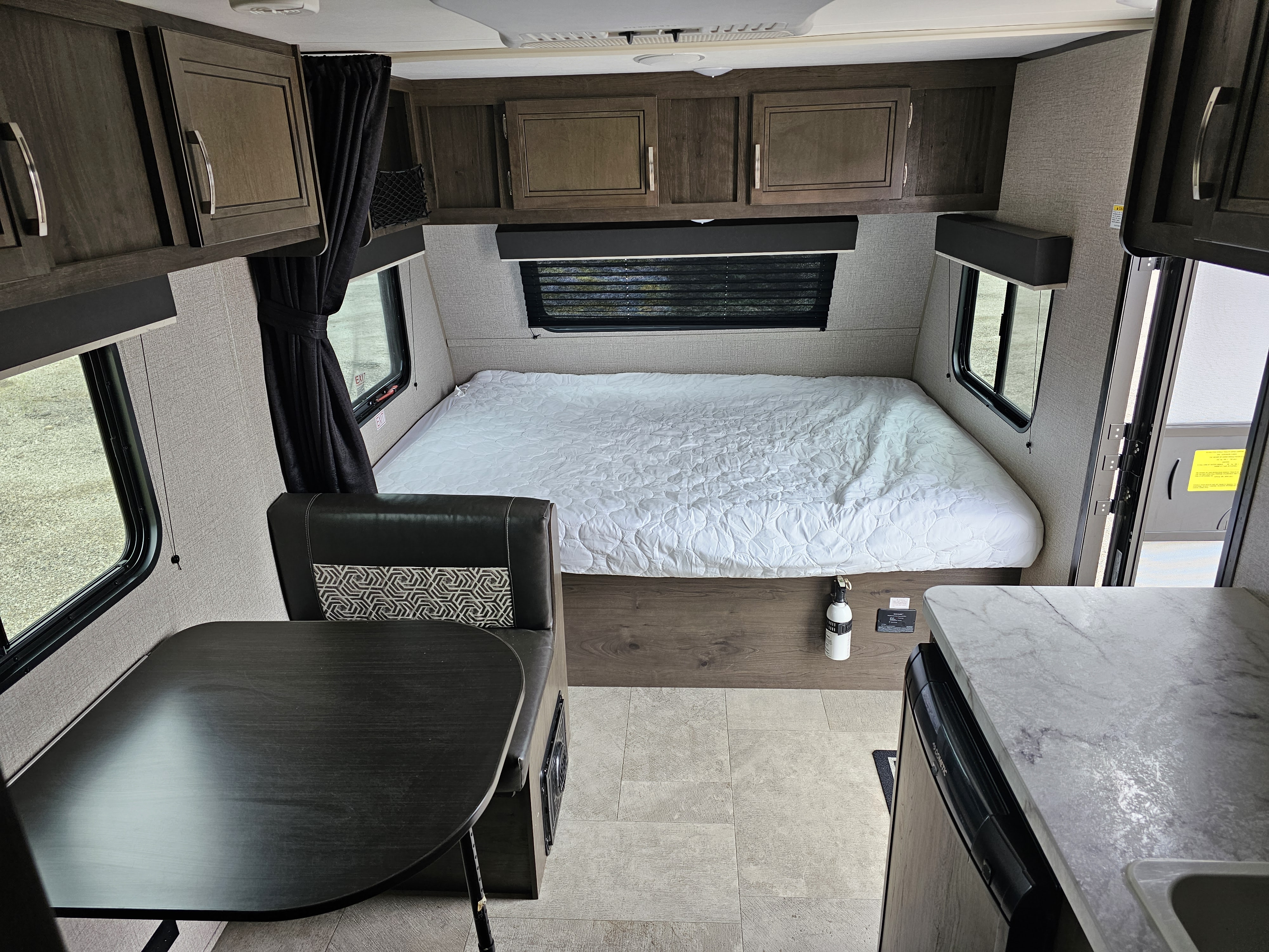 Inside this RV rental, see the dark wood cabinets above a white bed, a dinette on the left, and a compact kitchenette on the right.. Jayco Jay Flight 2020