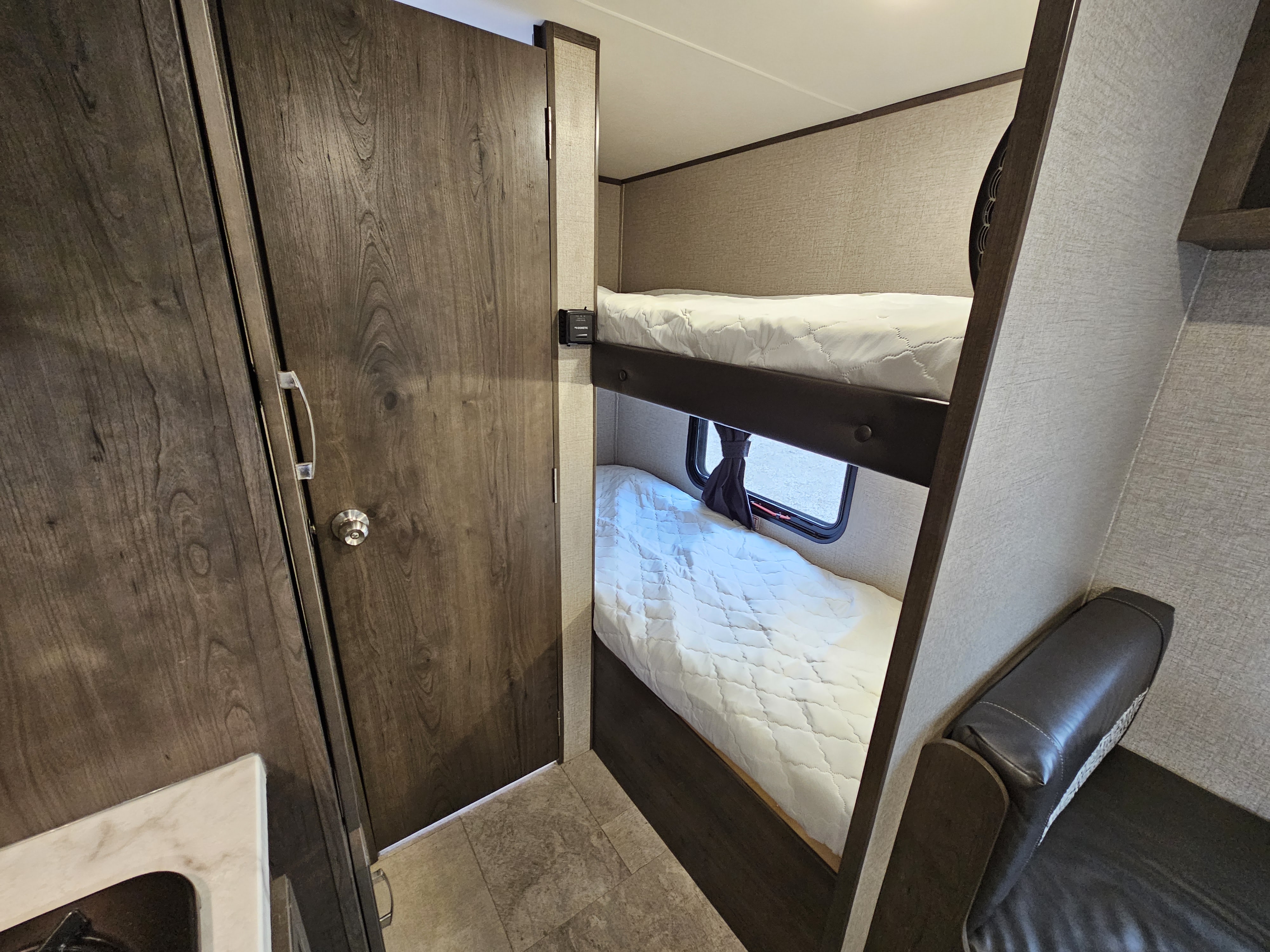 Cozy RV rental bunk bed area with textured walls and wooden door, ideal for compact living and family travel.. Jayco Jay Flight 2020